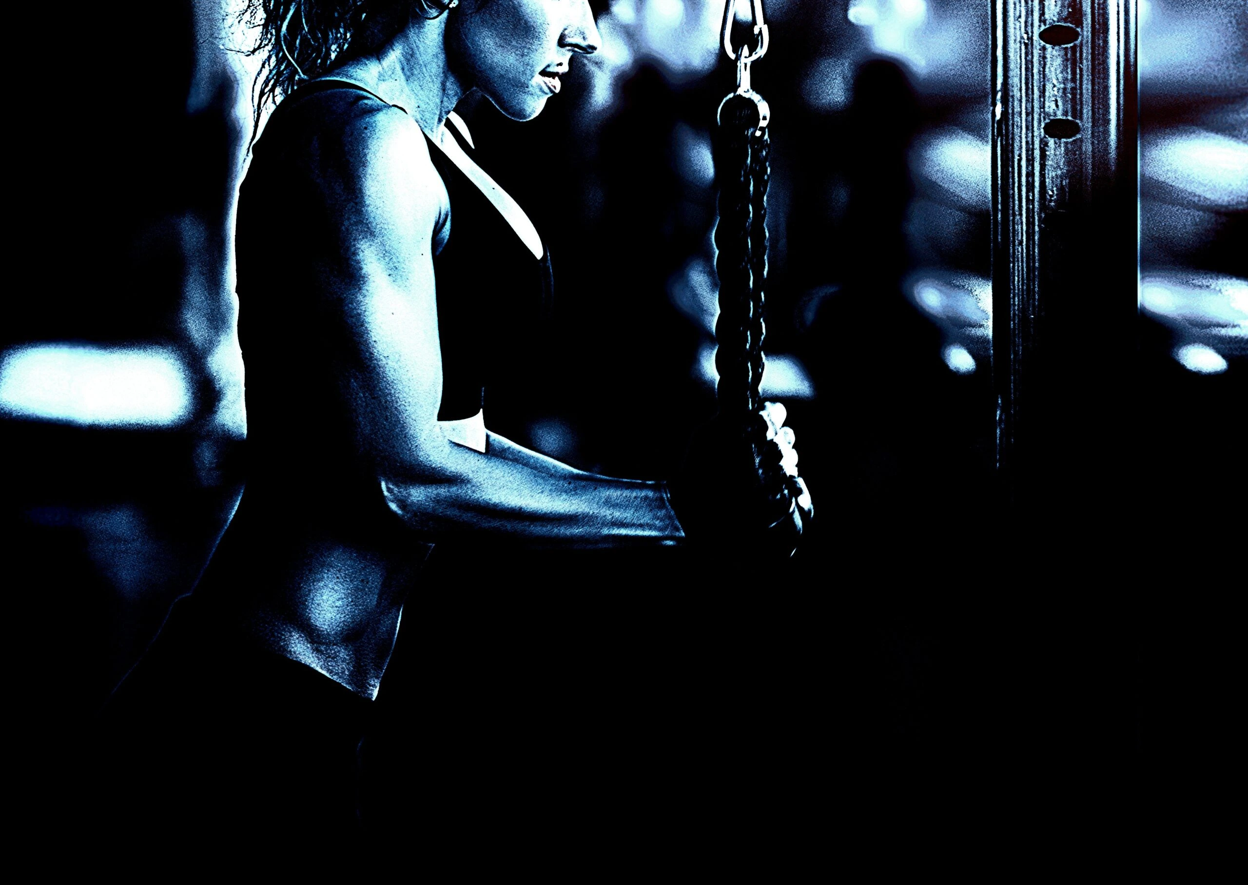 Close-up of a woman performing tricep exercises with a cable machine in a dark gym.