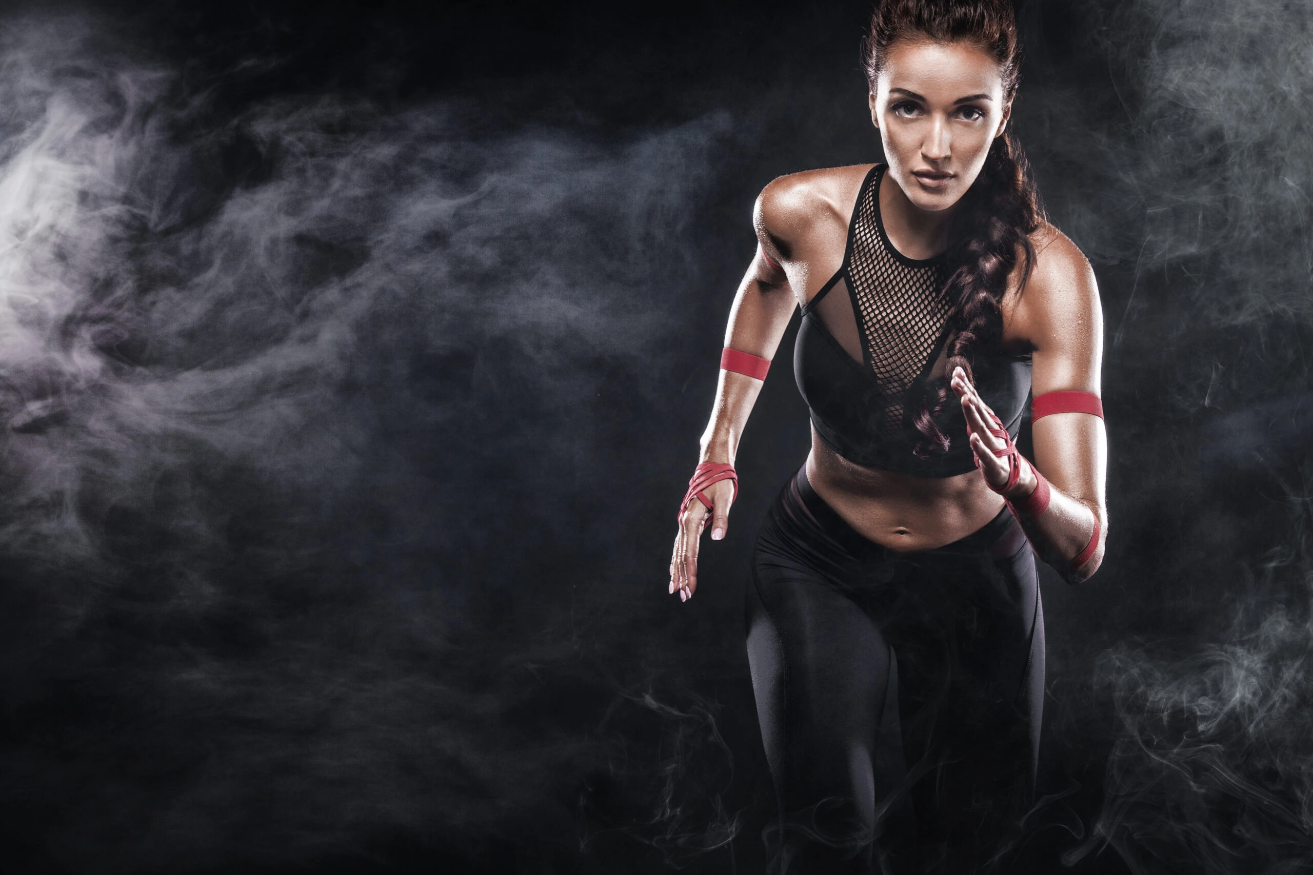 Fit woman in a black mesh sports bra running through a dark, foggy environment.