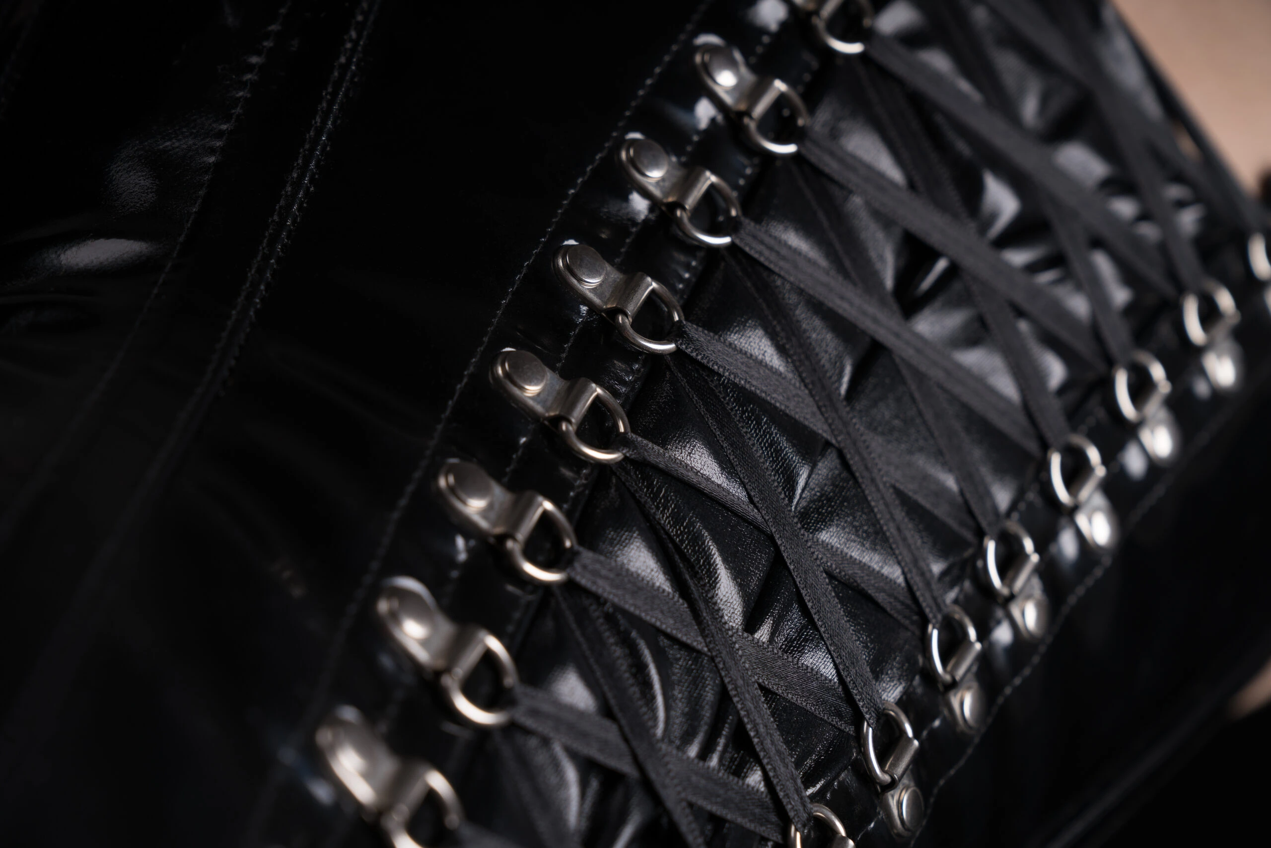 Close-up of corset lacing, focusing on the intricate loops and metal hooks of a black leather corset.