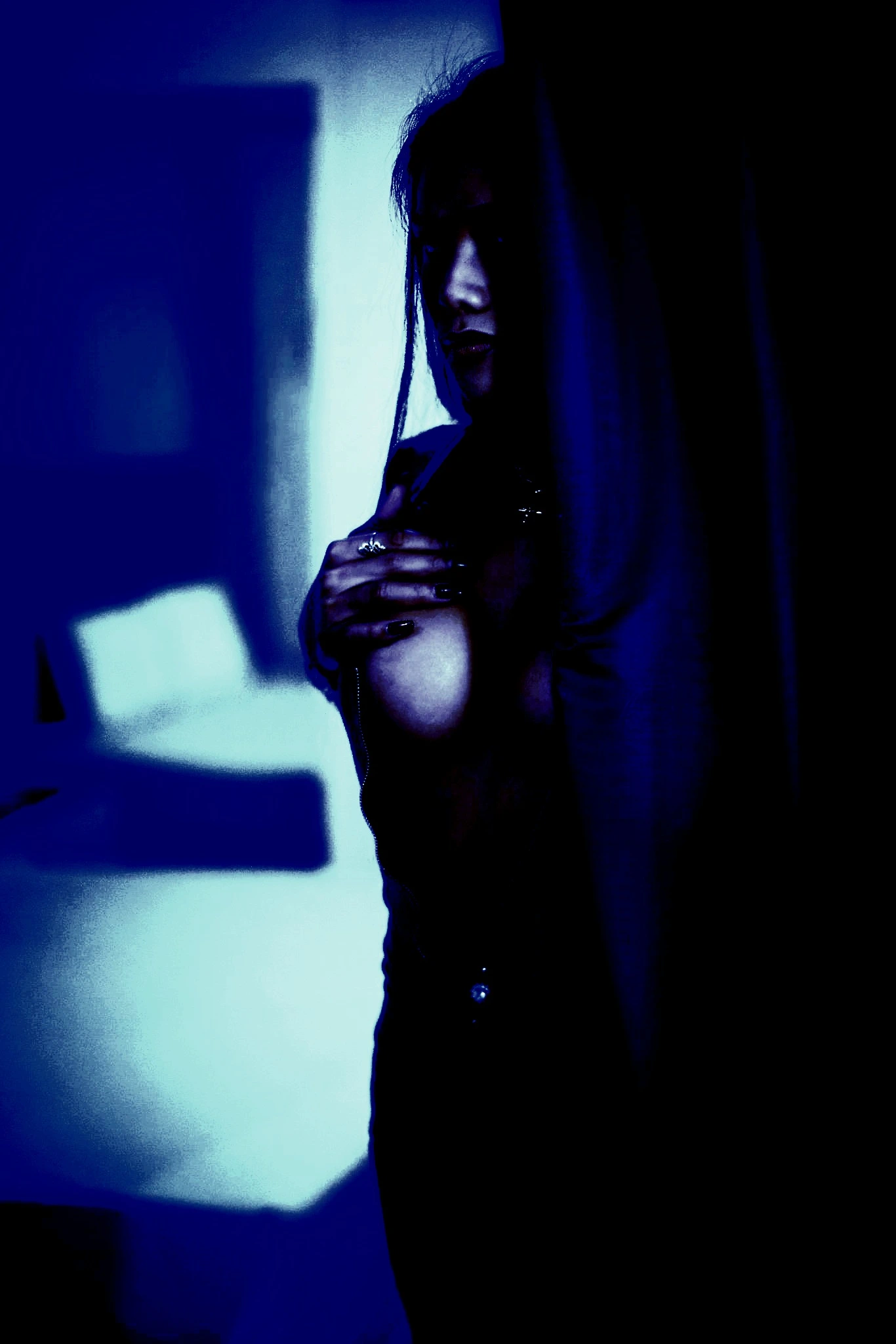 Woman partially hidden behind a curtain, lit with a blue hue, revealing part of her chest.