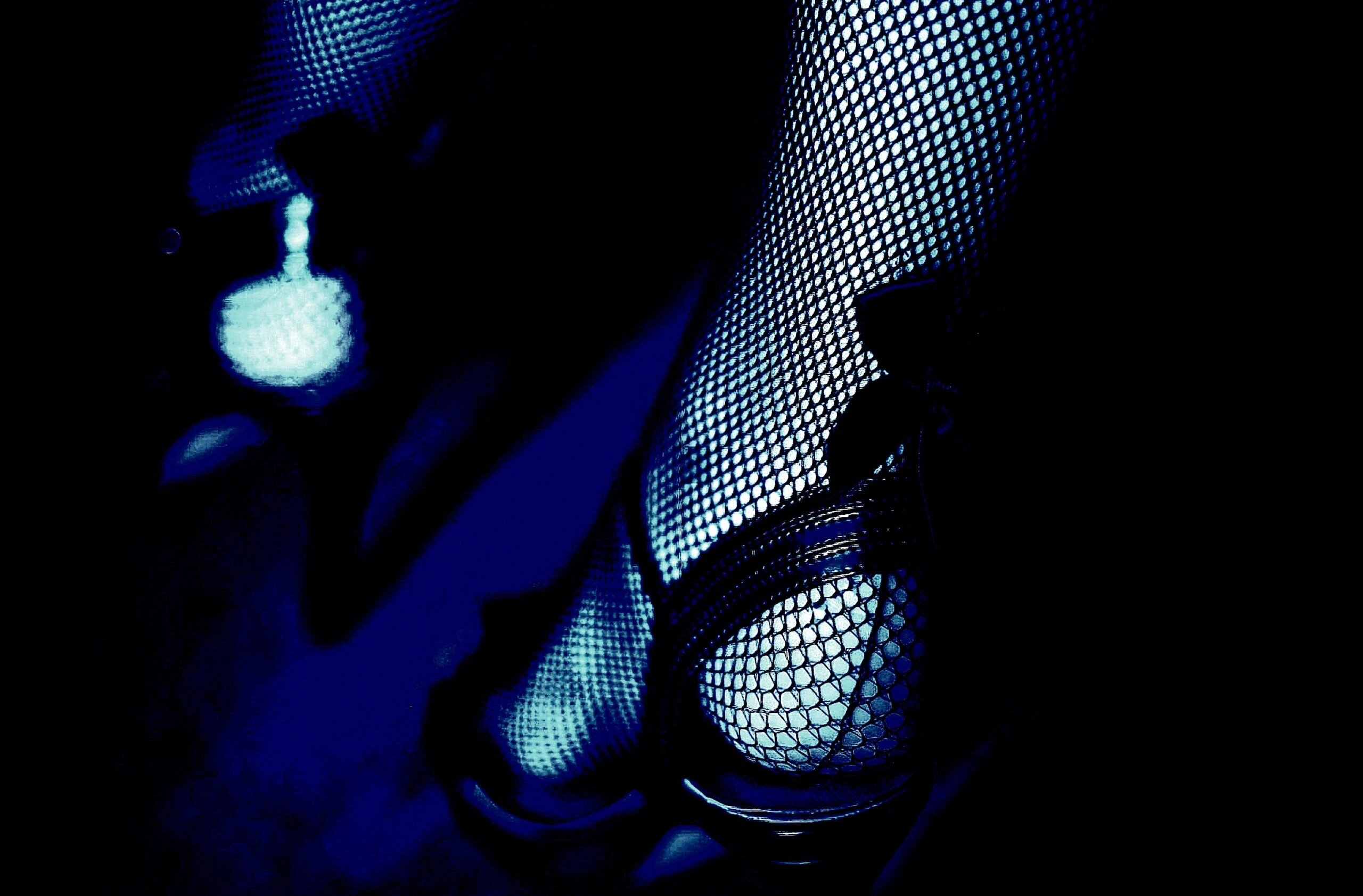 Close-up of fishnet stockings and high heels in a blue-tinted lighting.