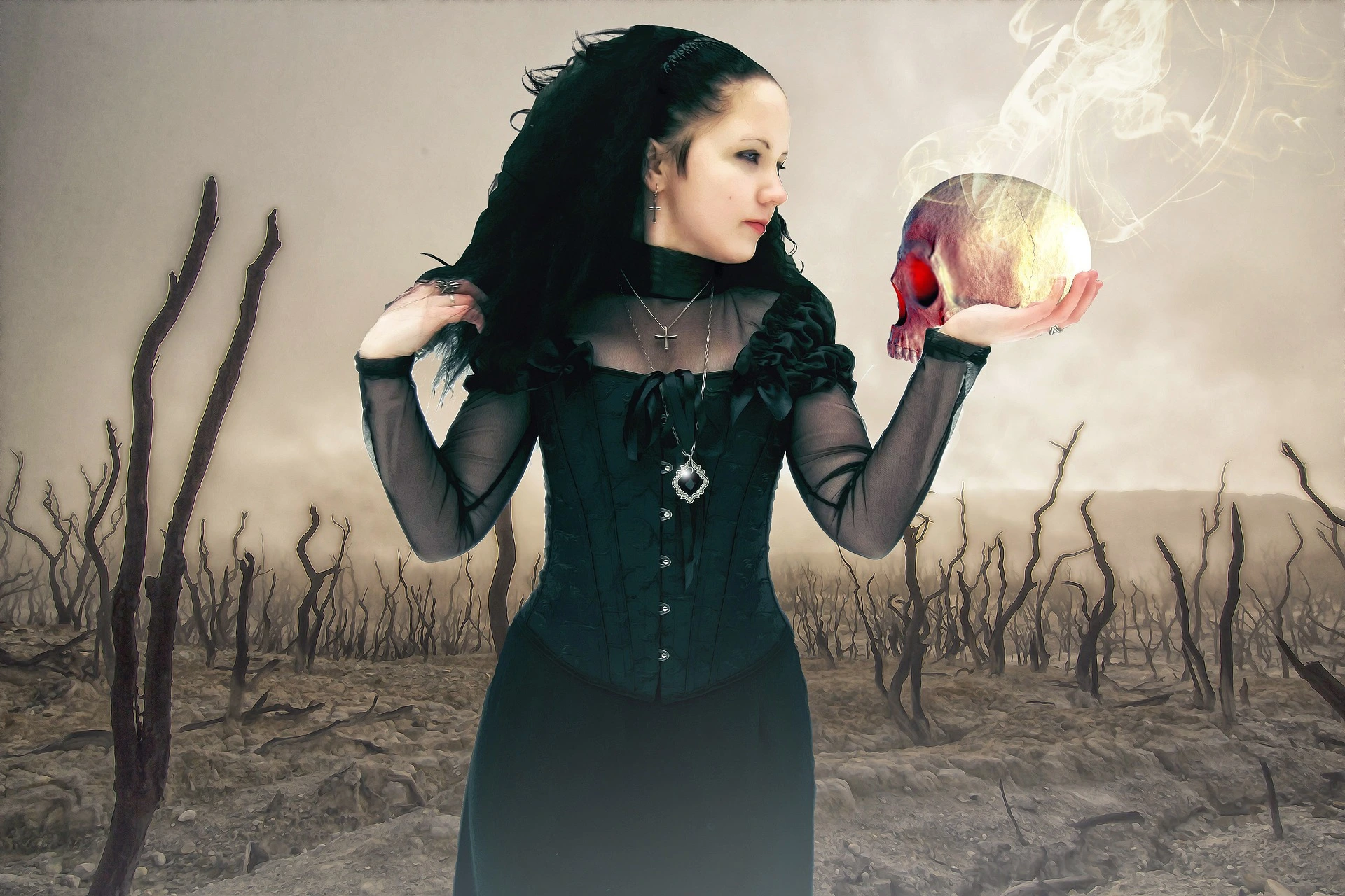 A gothic woman in a black corset holding a skull emitting red light and smoke, in a barren landscape with twisted, leafless trees.