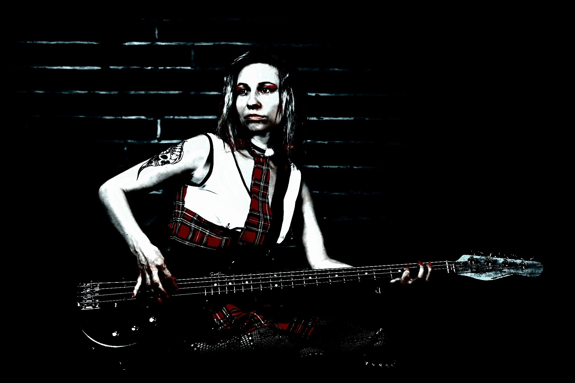 Gothic woman in red plaid outfit playing a bass guitar in a dark, moody setting.