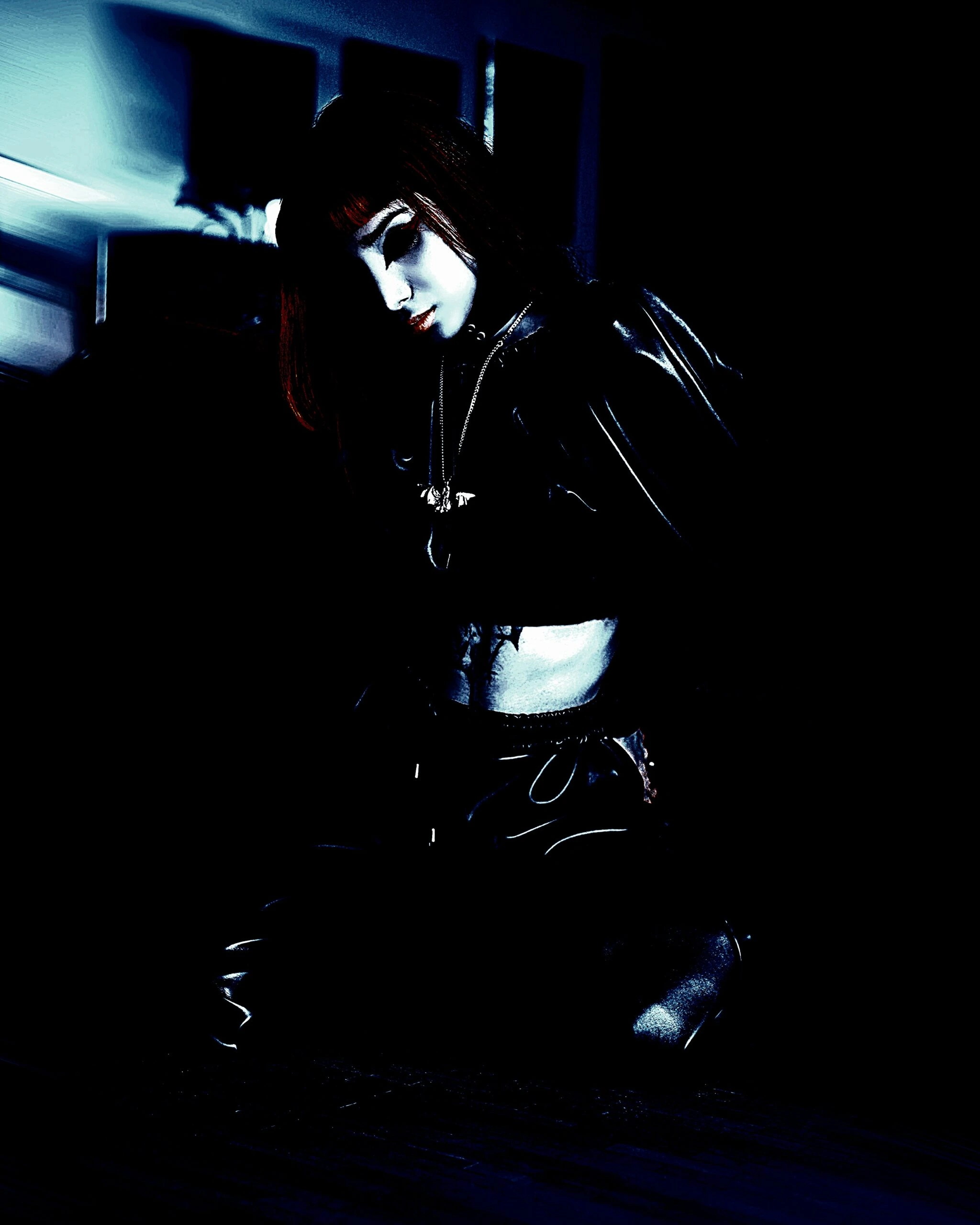 Dark, atmospheric photo of a goth cosplayer kneeling, with dramatic lighting highlighting the intricate costume details.