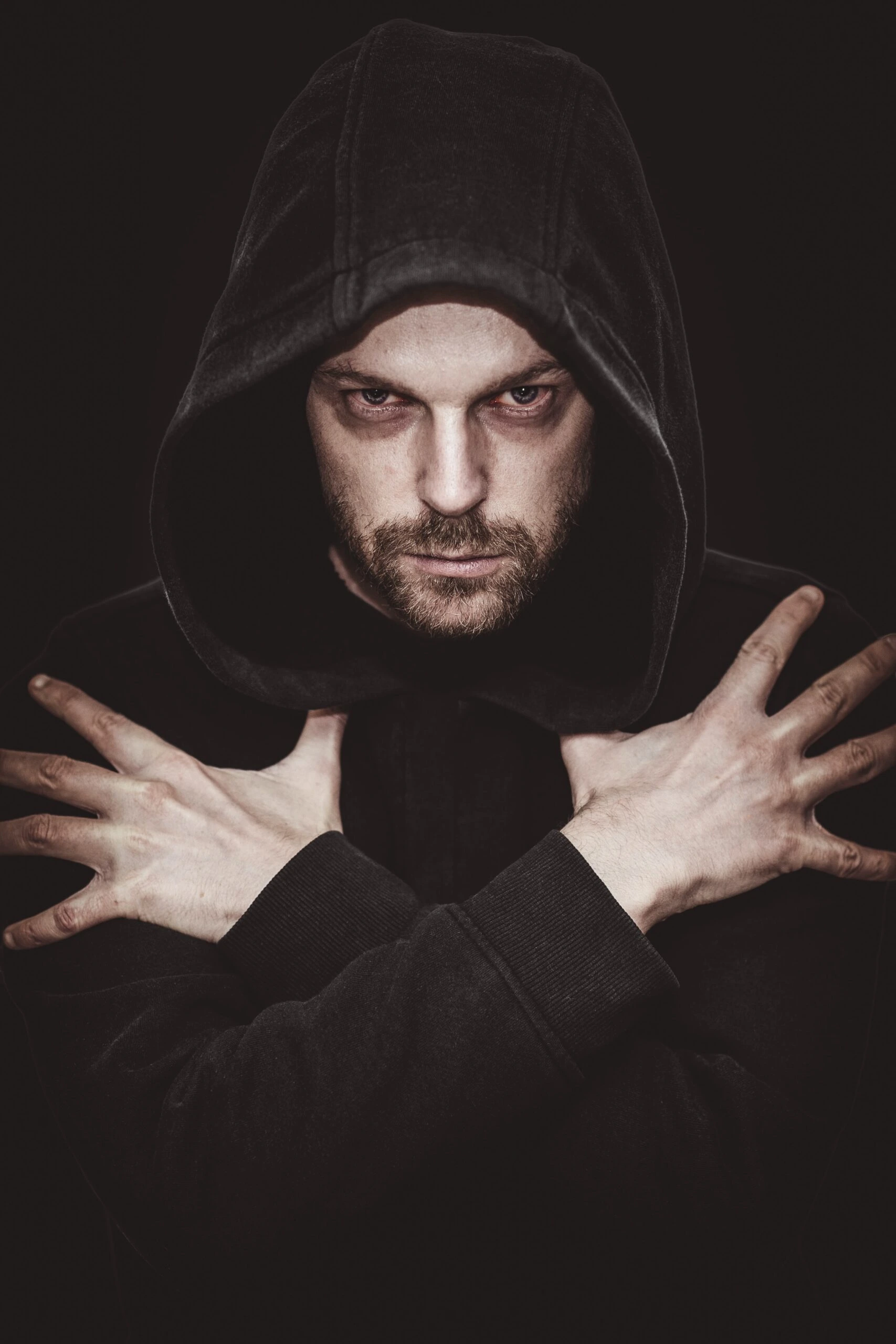 Brooding man with intense gaze, wearing a dark hoodie and crossing his arms in a vampire-like manner.