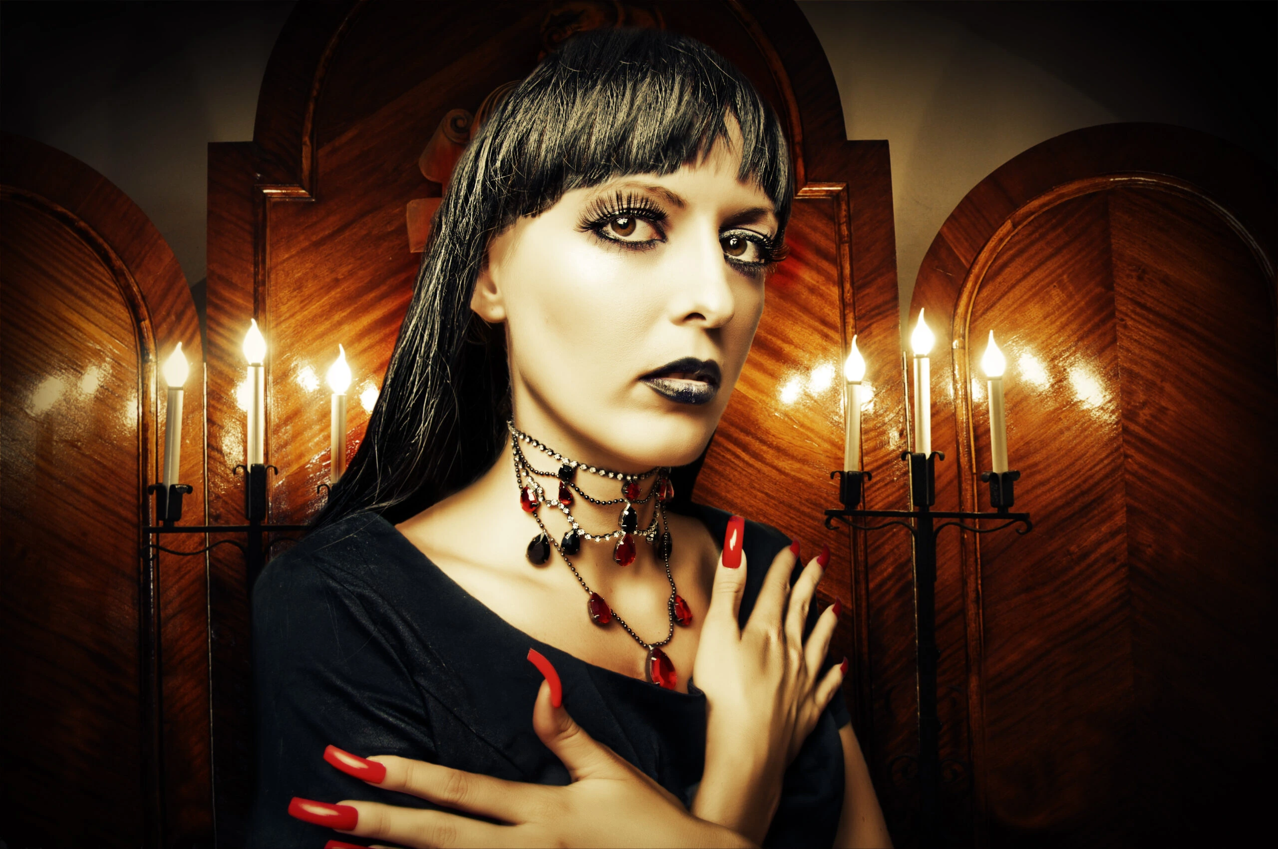 Gothic woman with dark makeup and spider web earrings, wearing a strappy top and choker necklace in a black-and-white photo.