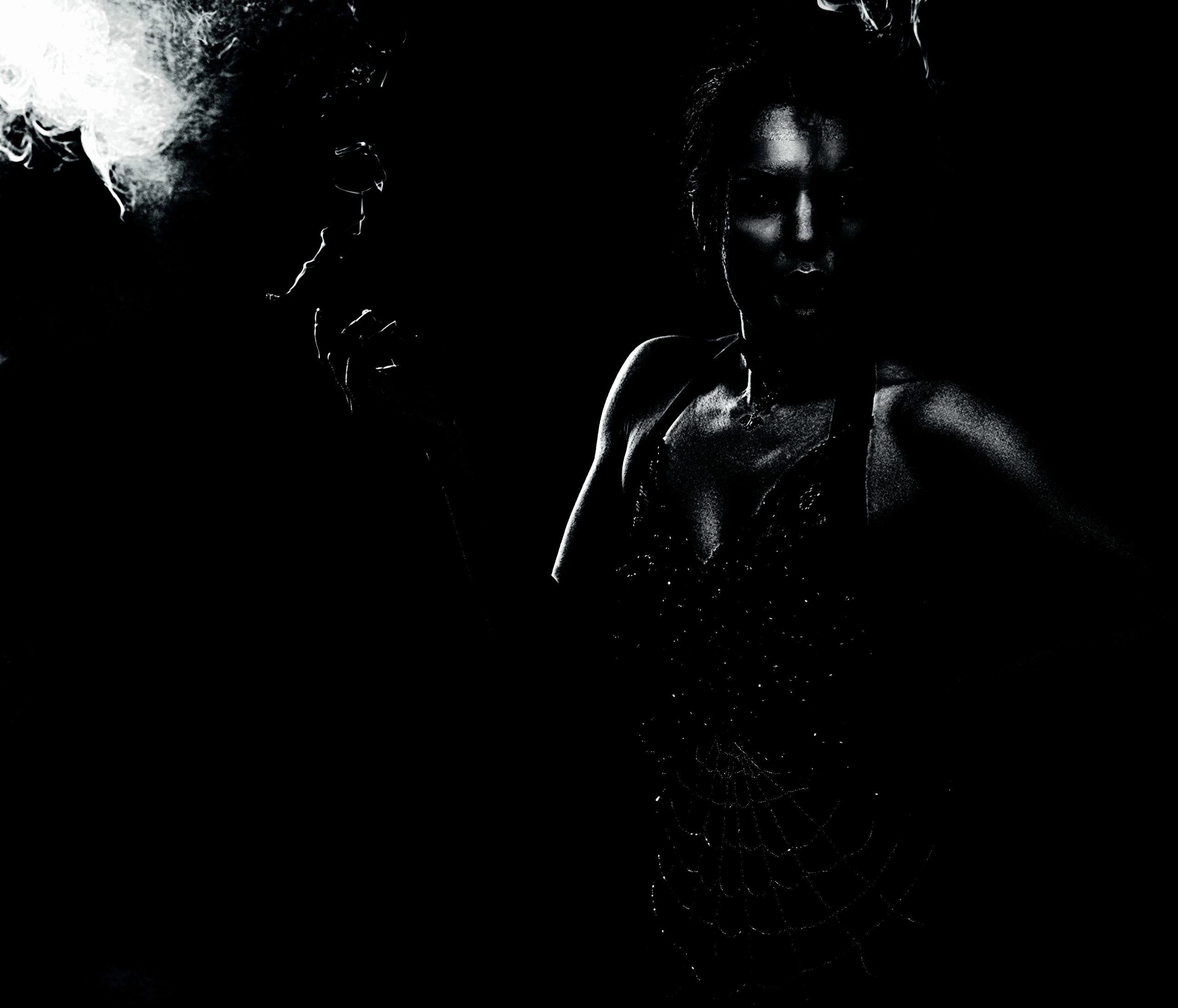 A woman in a gothic dress, her face and body partially obscured by smoke and shadows, creating a mysterious and dramatic scene.