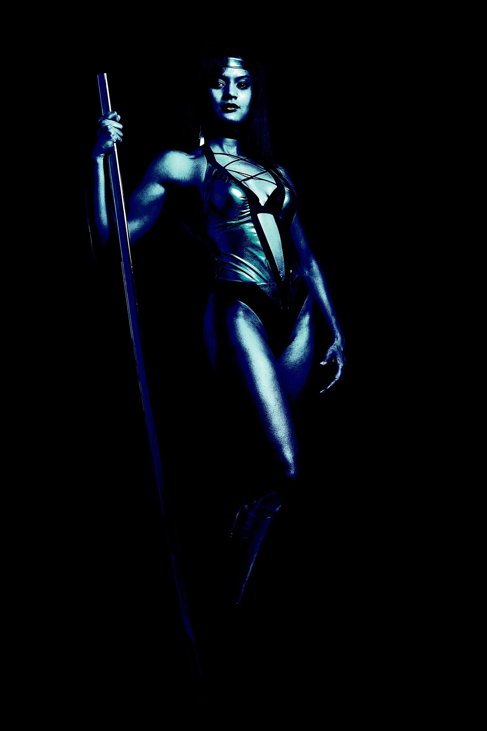 Metalhead cosplayer in a dark, metallic bodysuit, confidently holding a staff and standing tall in a dramatic pose.