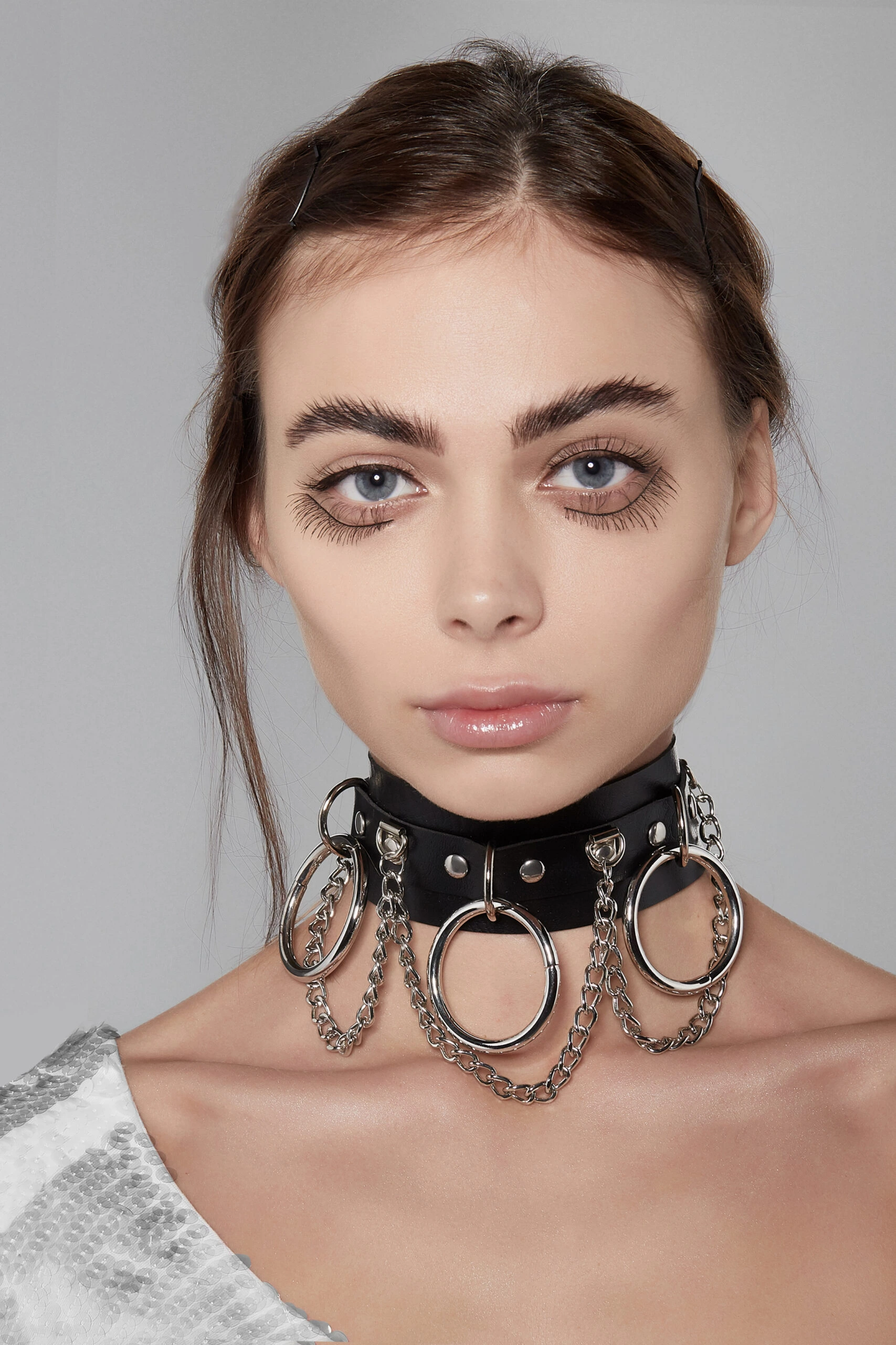 Woman with minimal makeup wearing a Gothic choker with multiple metal rings and chains.