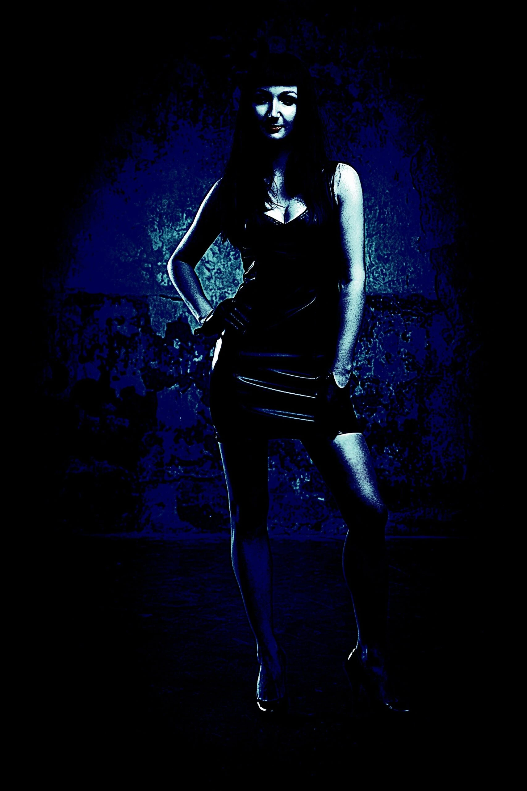 A woman in a dark, edgy dress stands confidently against a textured background with a strong contrast of deep blues and blacks, evoking a moody gothic atmosphere.