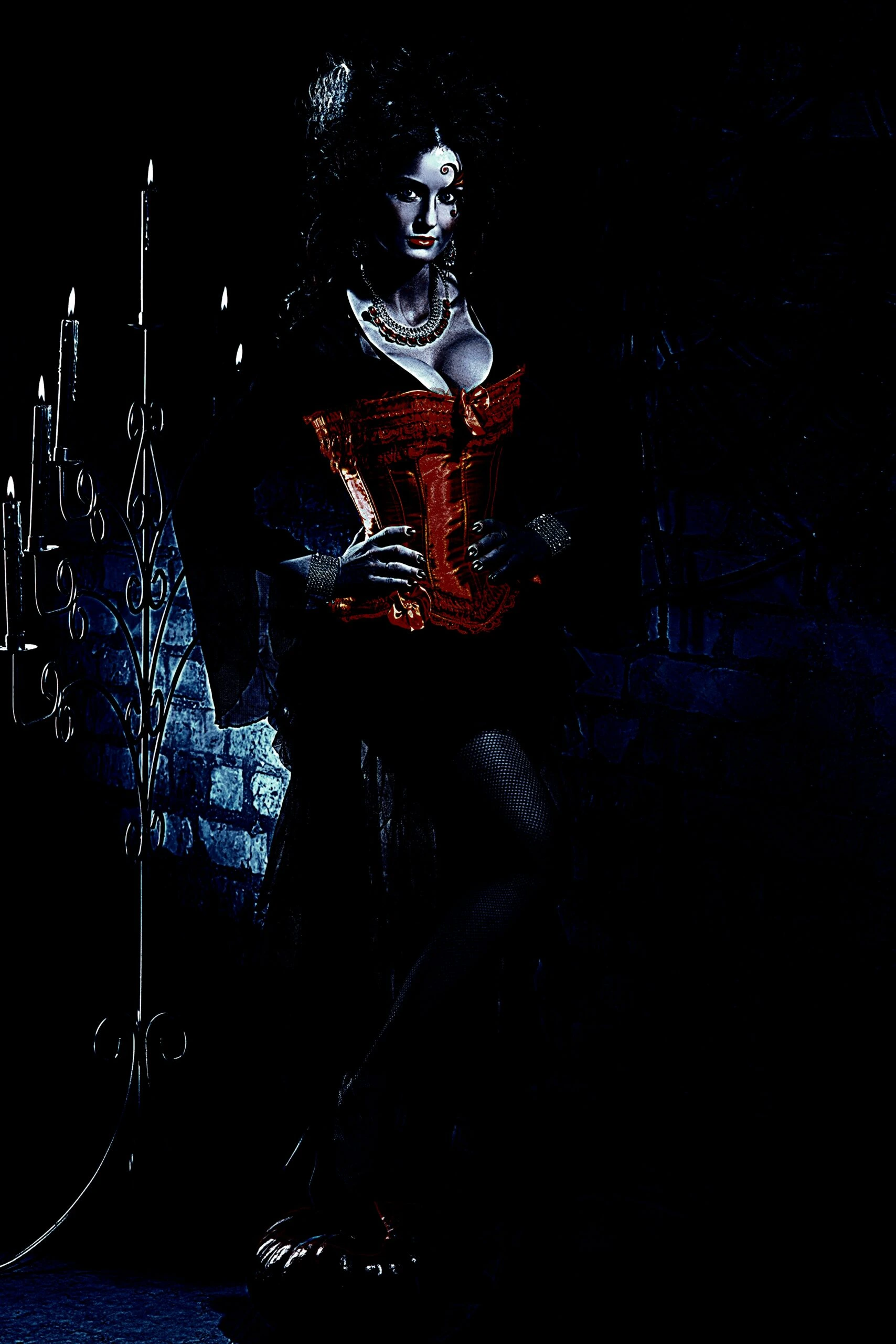 A gothic woman wearing a striking red corset, standing against a dimly lit wall with a tall candelabra casting a haunting glow. 