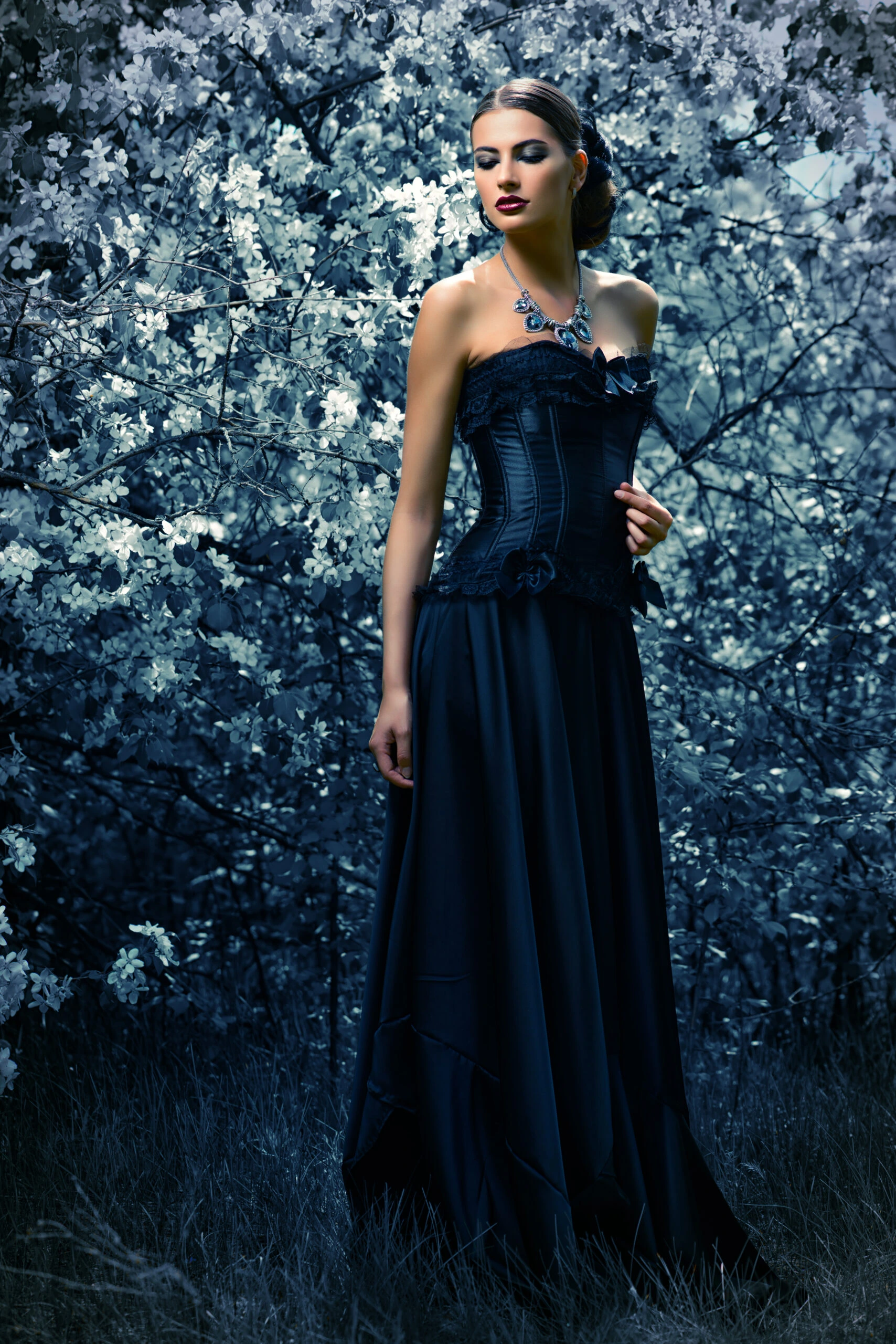 Gothic woman in a long black dress with a corset, standing in a blooming dark forest, evoking a mysterious and ethereal atmosphere.