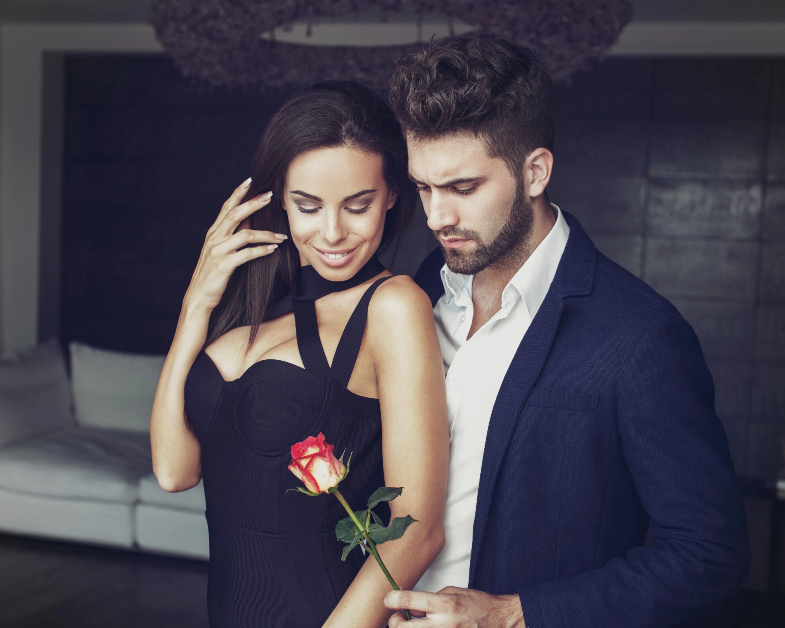 Confident woman dressed in lingerie holding a whip, standing next to a man wearing jeans and an open shirt.