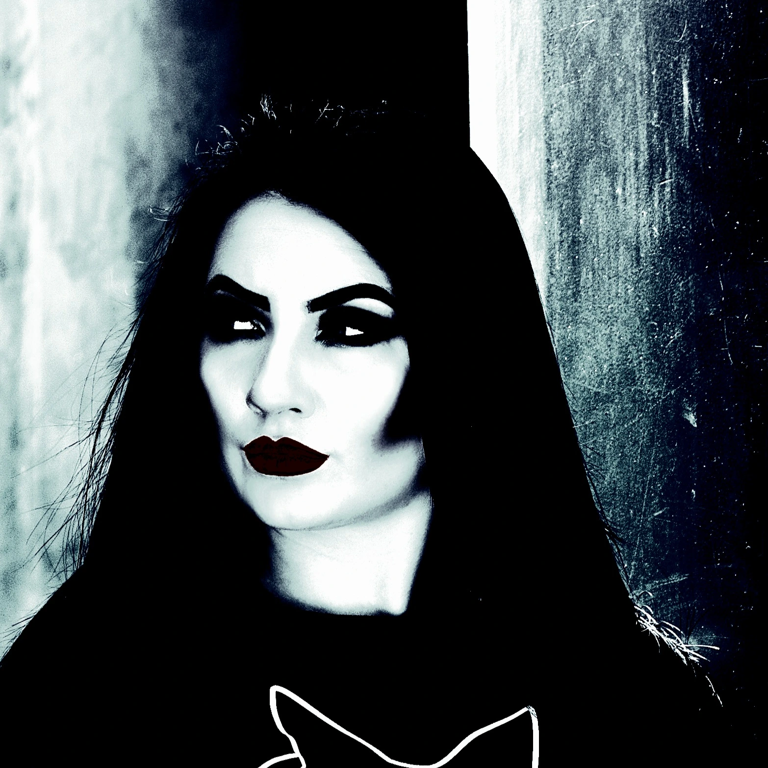 Close-up of a woman with dramatic makeup, dark hair, and red lipstick against a dark, shadowy background.