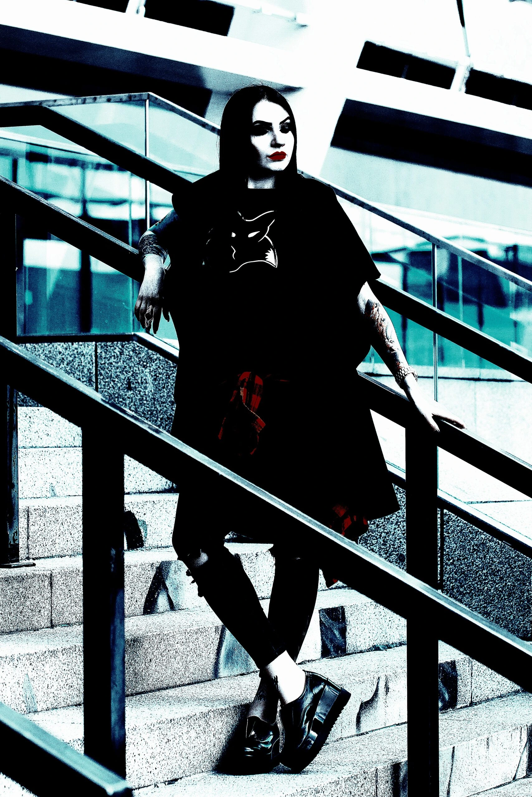 Woman with dark hair wearing a black outfit, leaning on a stair railing, with a confident pose in an urban setting.