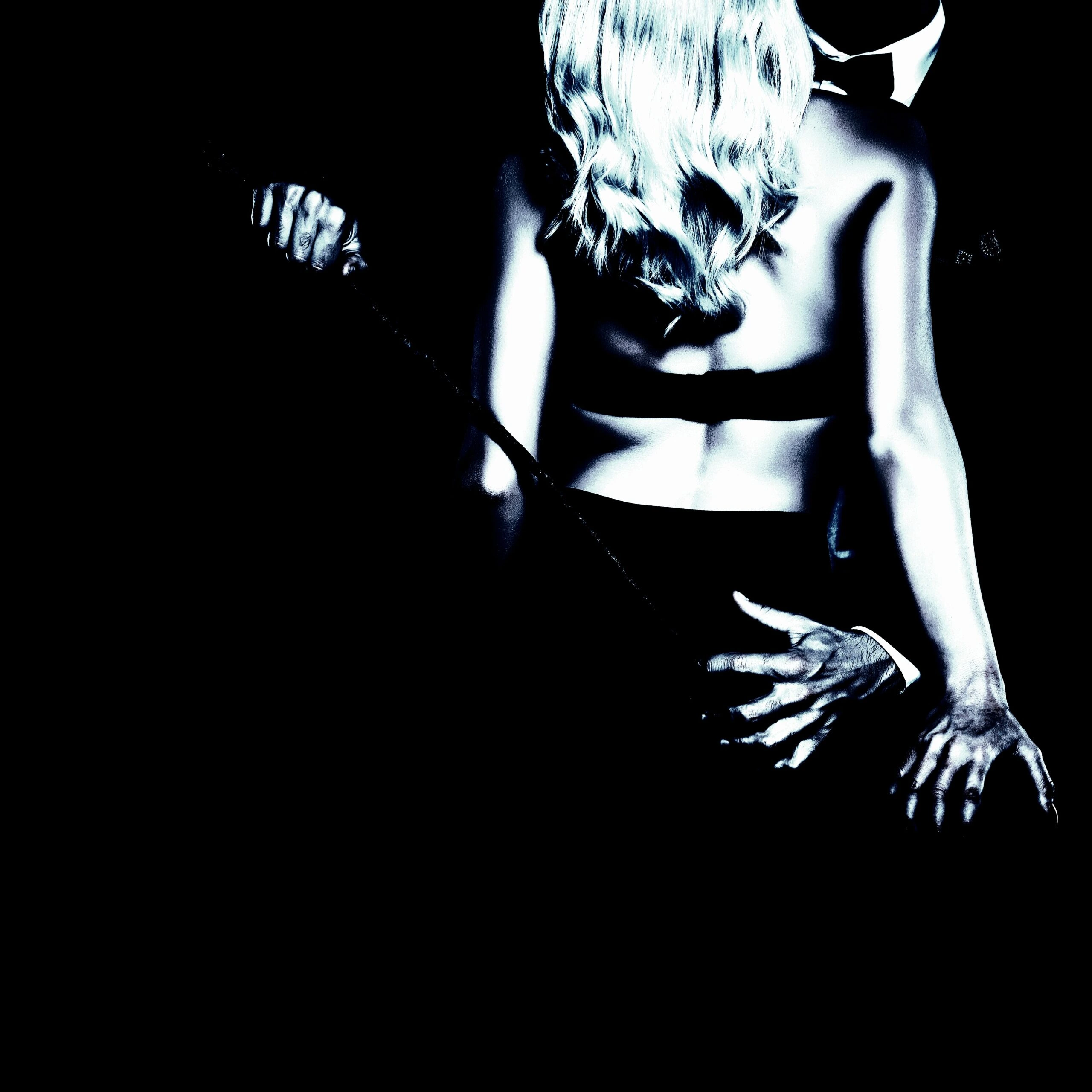 Couple in an intimate embrace, the woman in lingerie and the man in a suit, holding a whip.