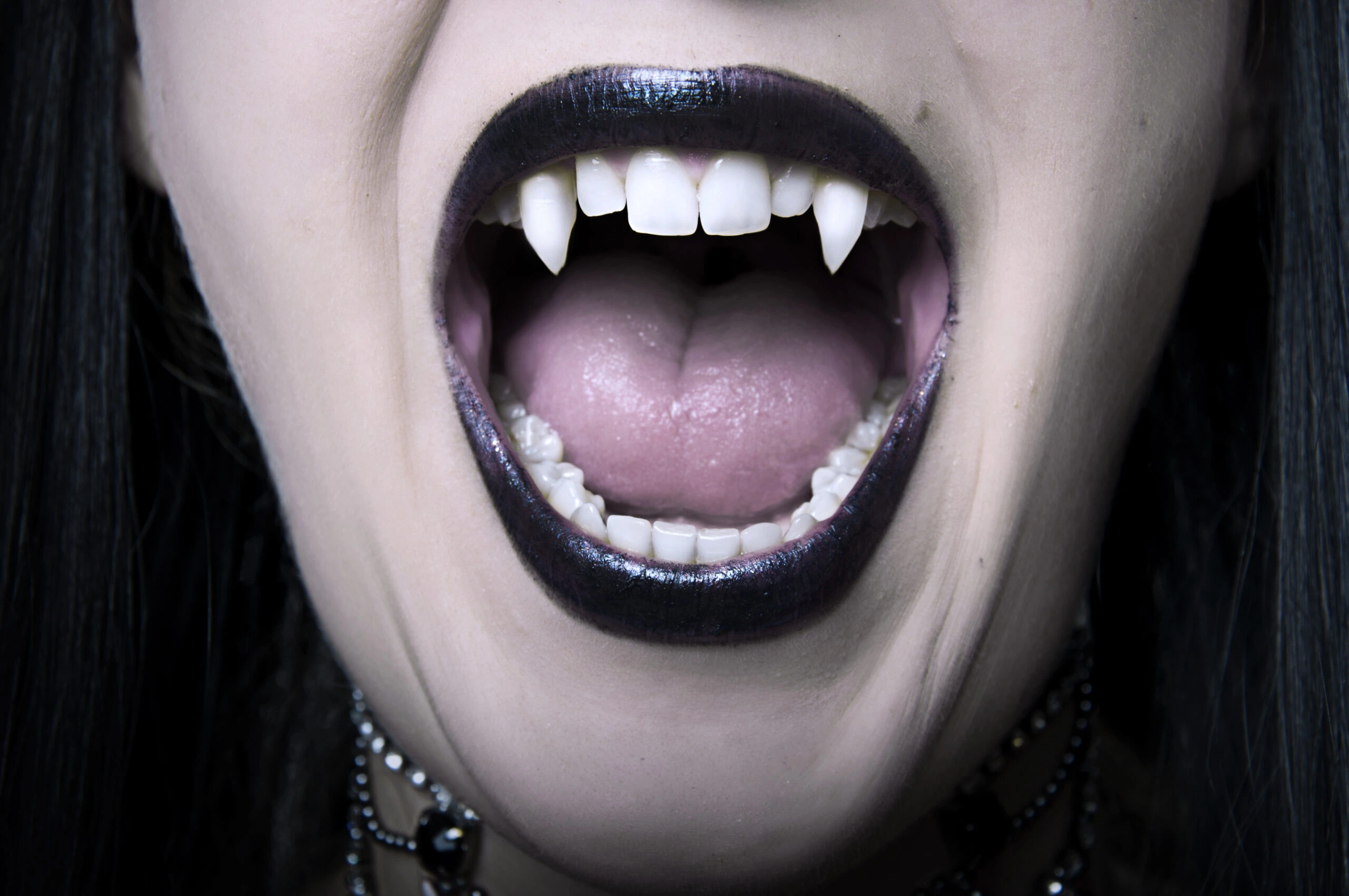 Close-up of a vampire's mouth with sharp fangs and dark lipstick.