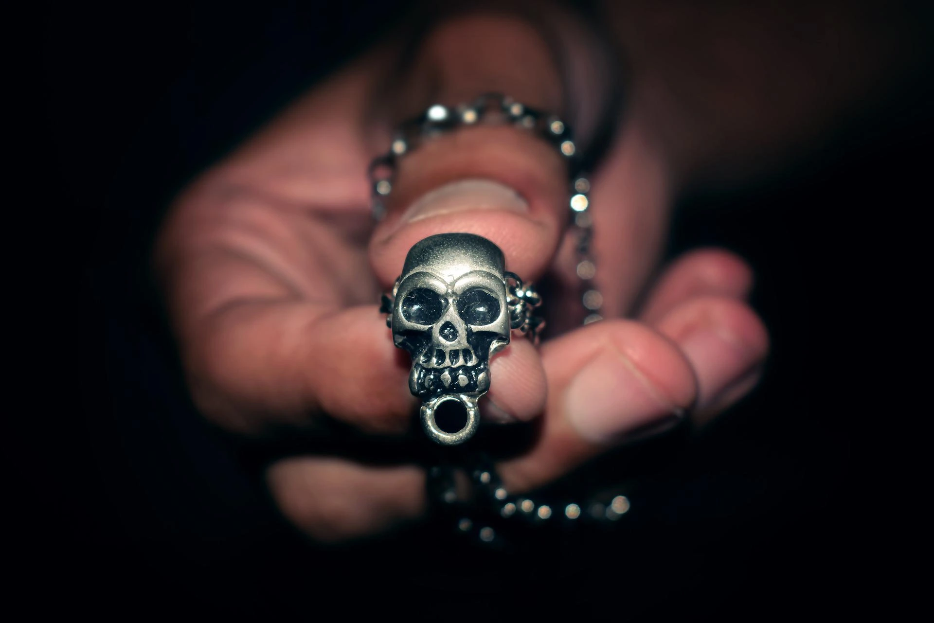 Close-up of a hand holding a Gothic skull pendant necklace.