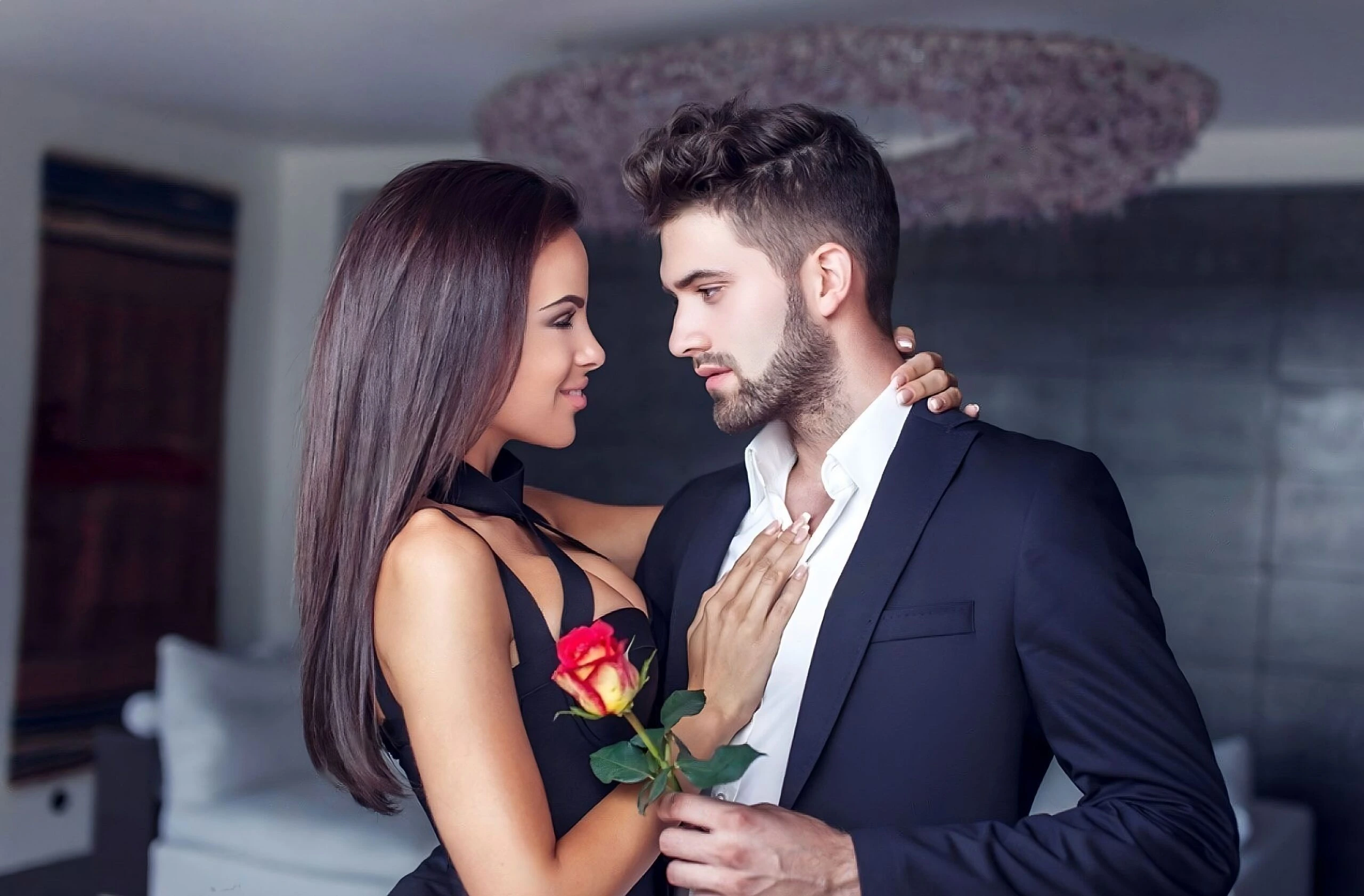 Stylish couple dressed for a night out, sharing a tender moment with a red rose 