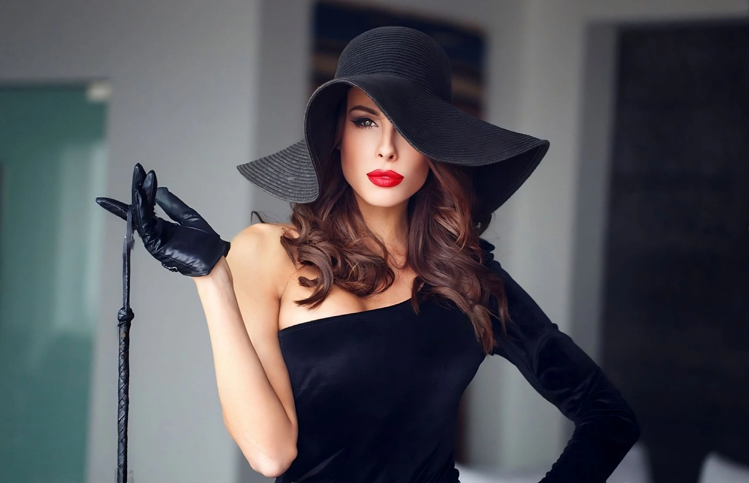 Elegant woman in a black dress and hat holding a riding crop, exuding confidence and allure