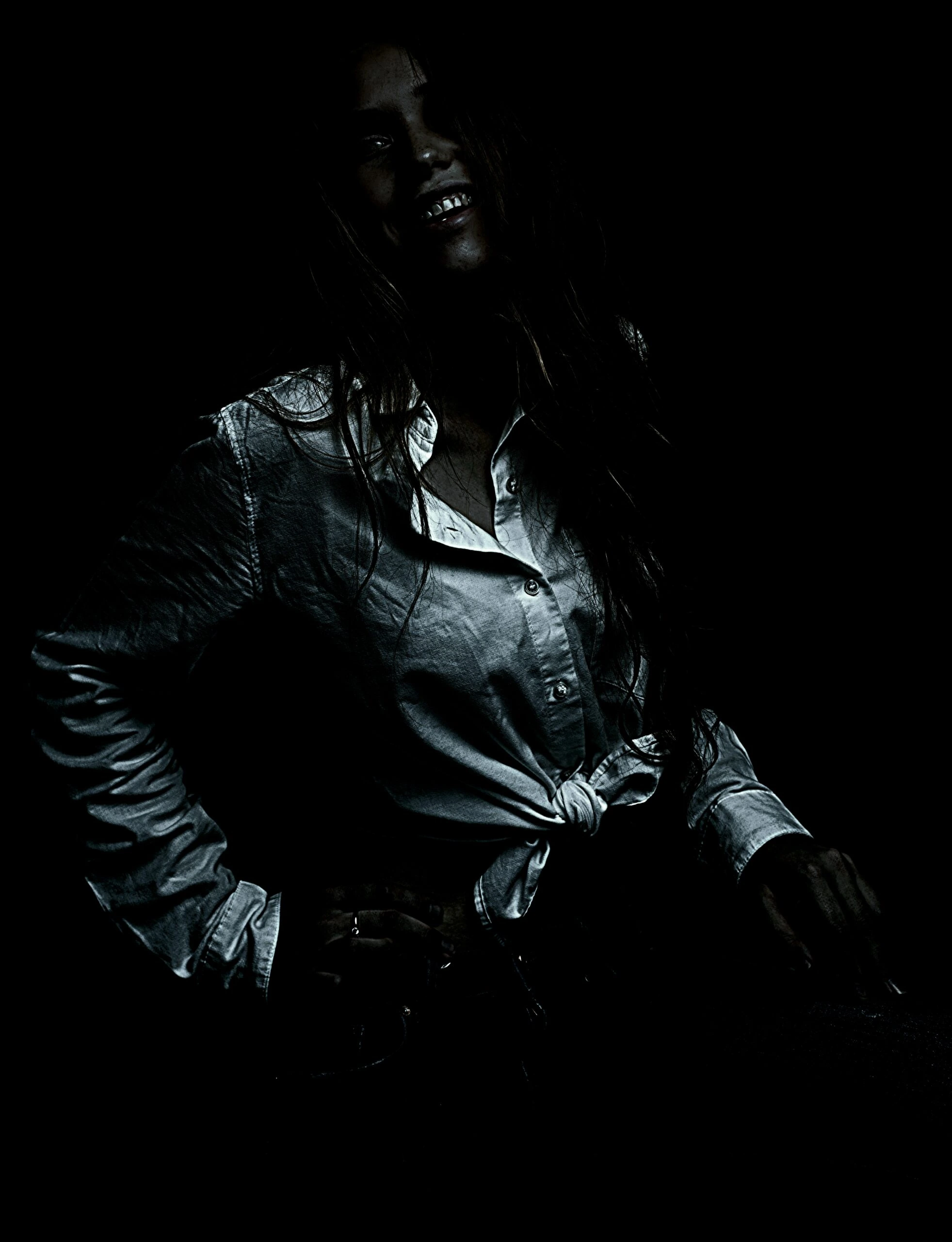 Woman in a dark setting, wearing a tied button-up shirt and jeans.