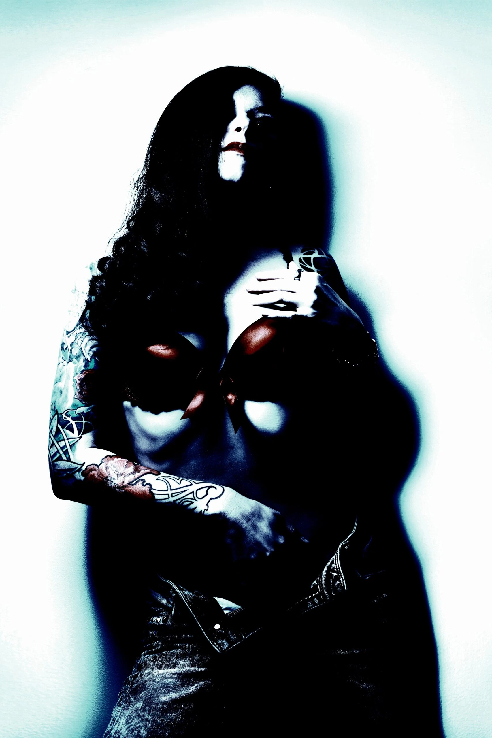 Gothic woman with tattoos and a red bra, posing dramatically against a white wall.