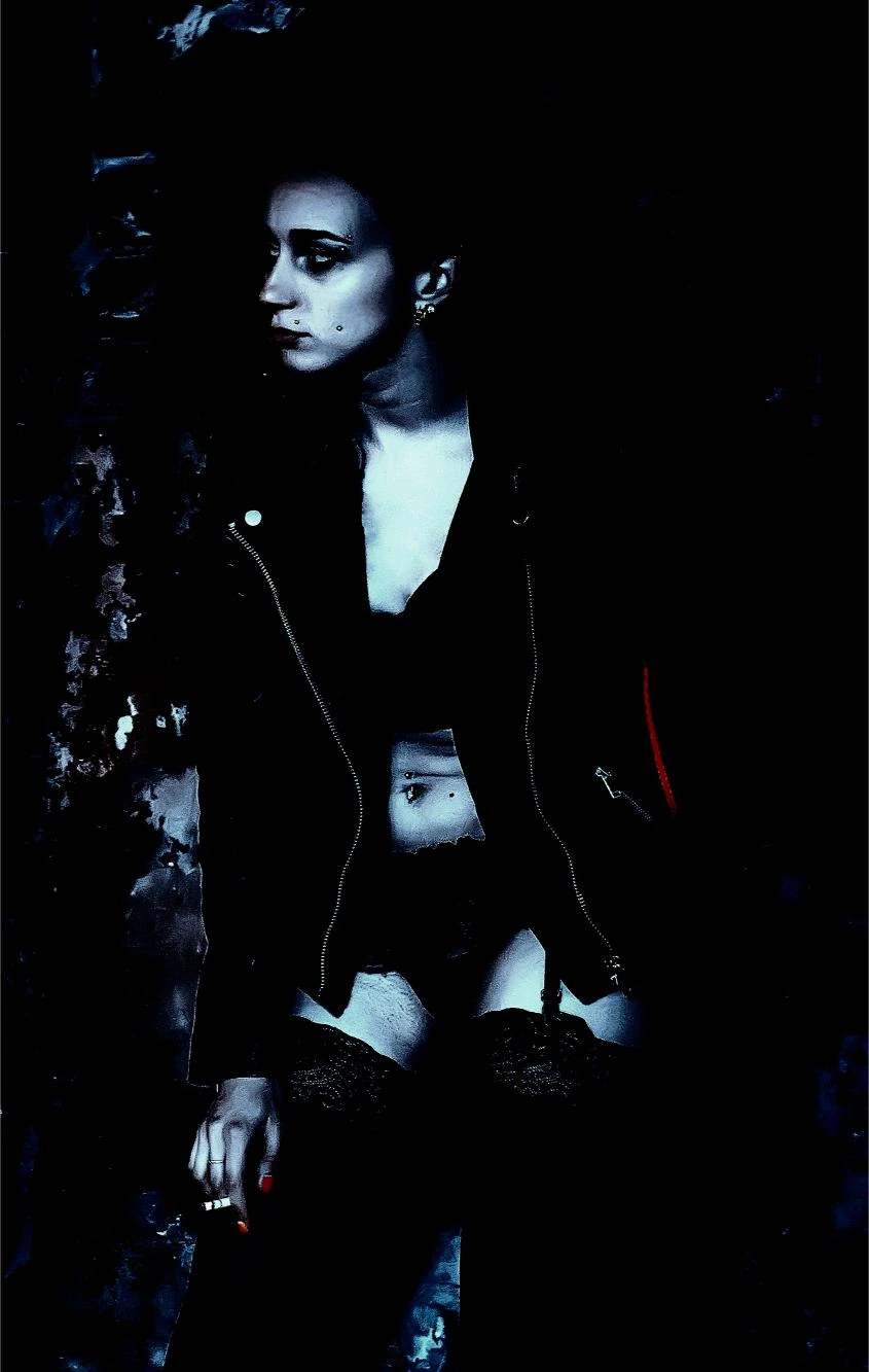 Gothic woman in dark clothing with piercing gaze, framed in shadows for a mysterious, intense aesthetic.