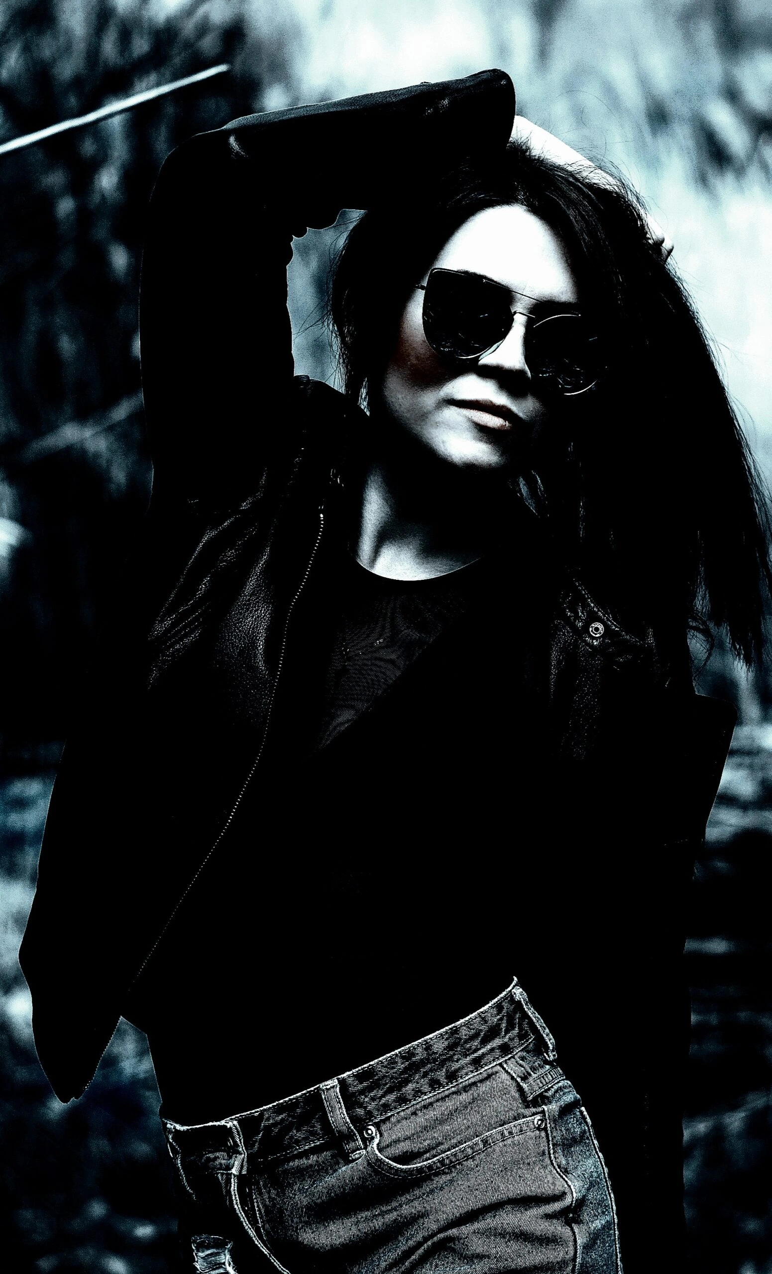 Woman in a black outfit with a fierce expression, standing in a dimly lit gothic setting.