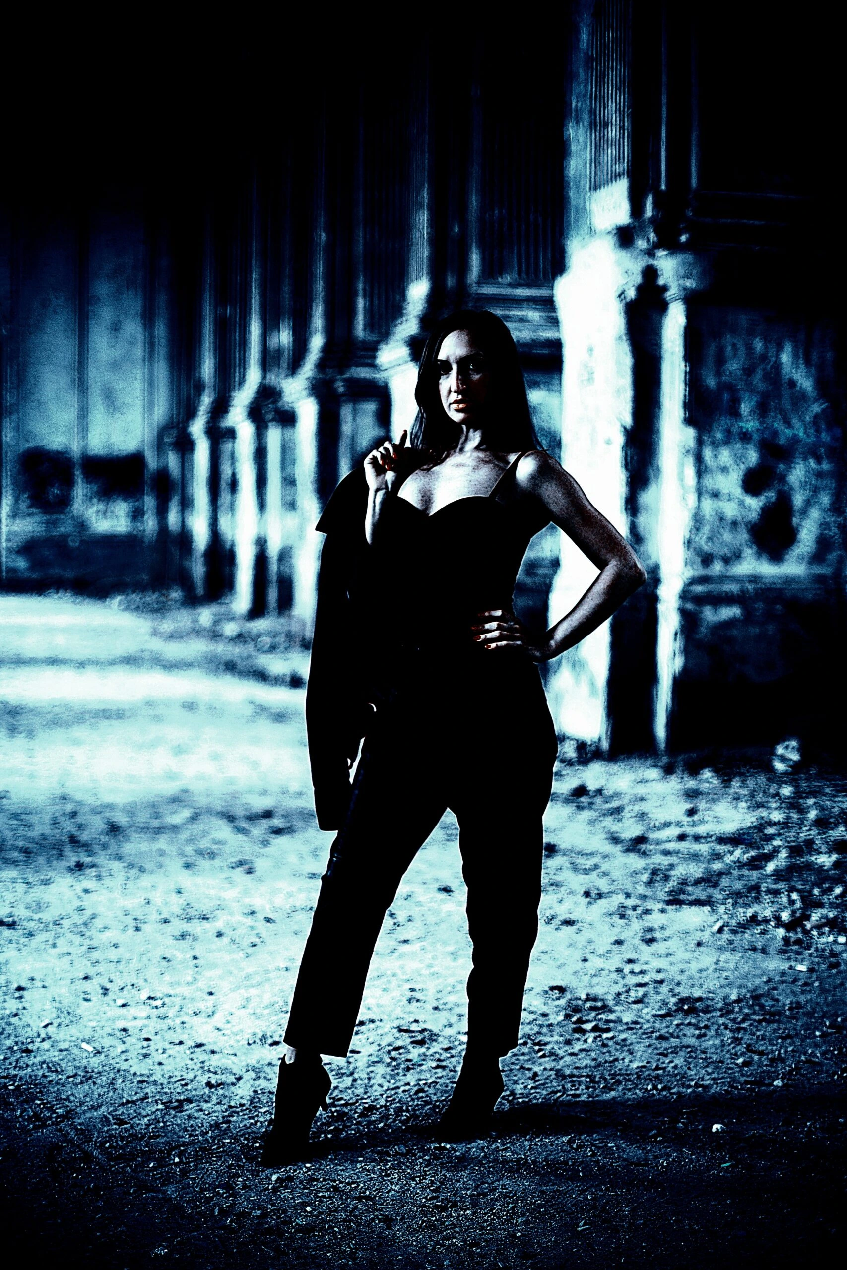 Woman in black outfit standing confidently in a gothic architectural setting, bathed in a blue tint.