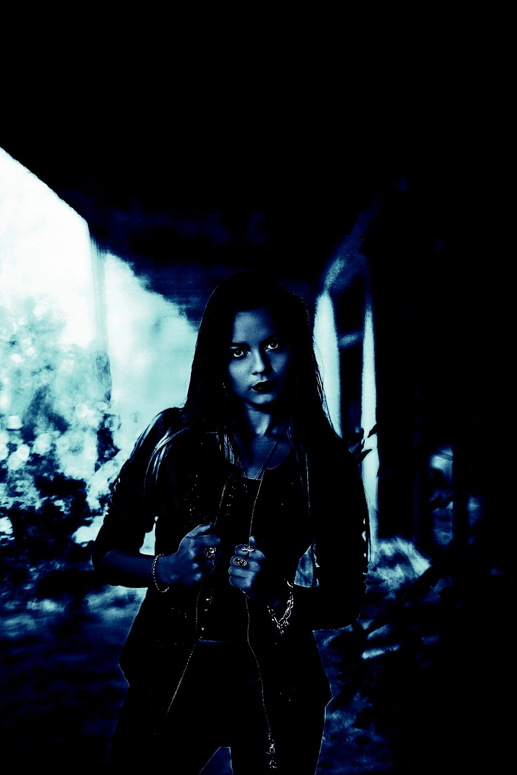 Gothic woman in a leather jacket, leaning against a tree, with a contemplative expression, in a blue-toned scene.