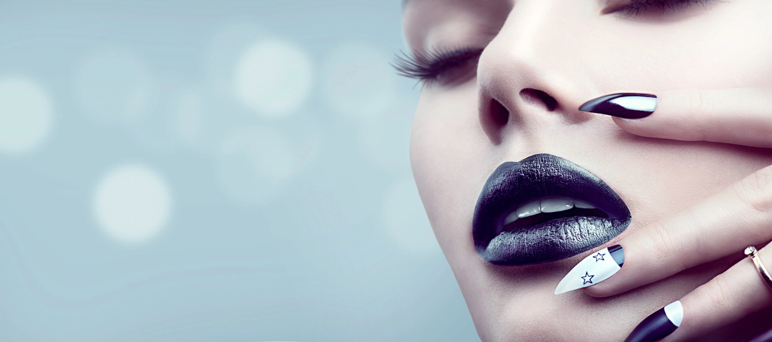 Close-up of a woman with dark lipstick and star-themed nails, capturing a gothic makeup look.