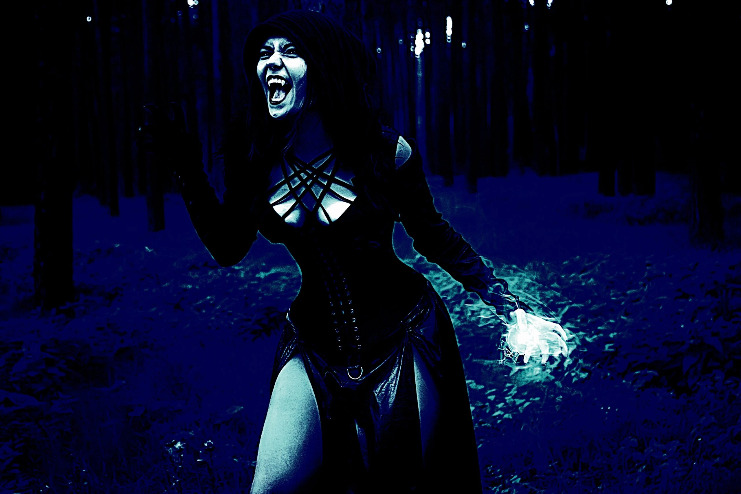 Woman in a gothic black dress with a dramatic expression, holding a magical light in a dark forest.