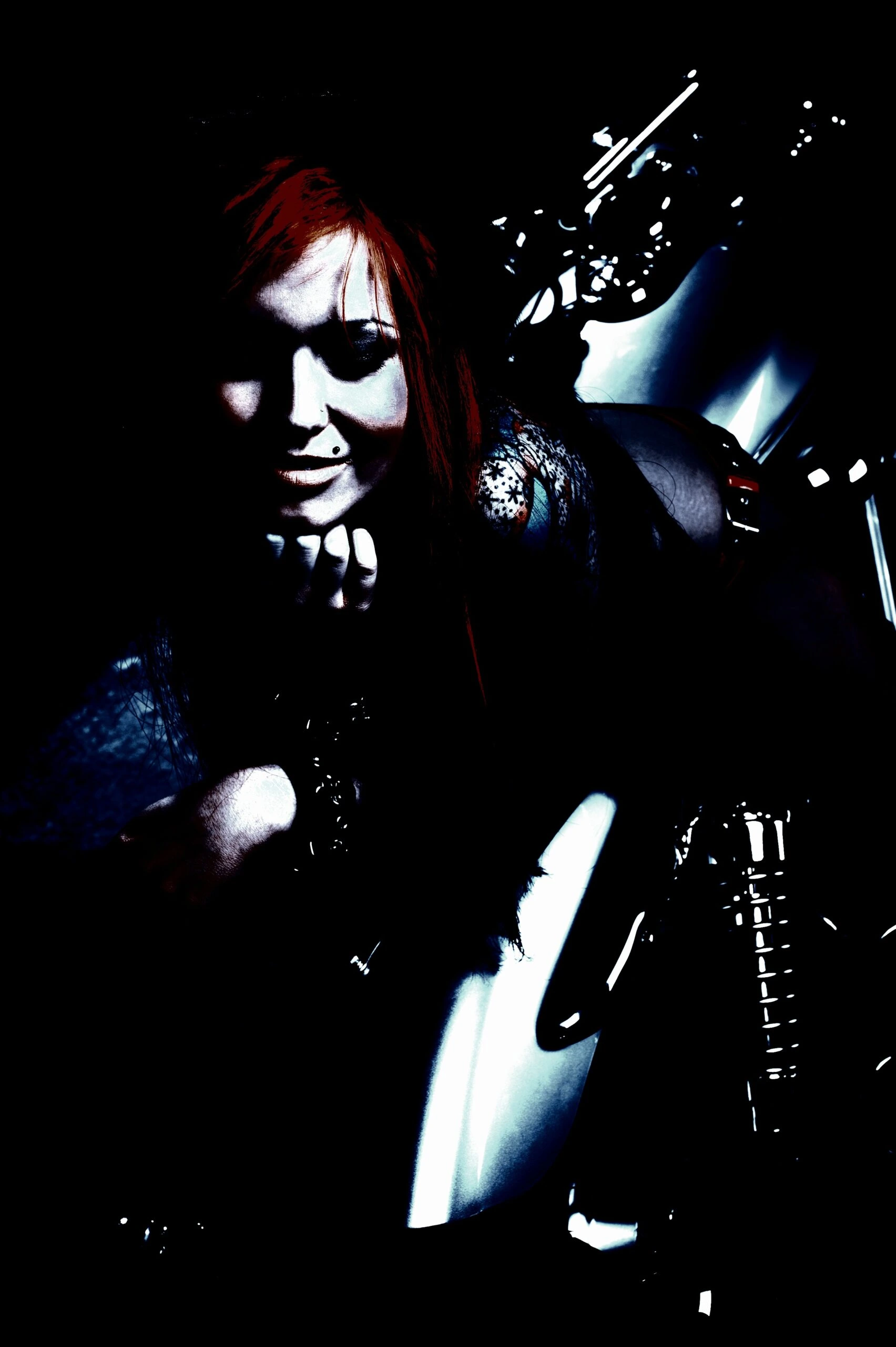 Smiling gothic woman with red hair and tattoos, in a dark, moody setting.