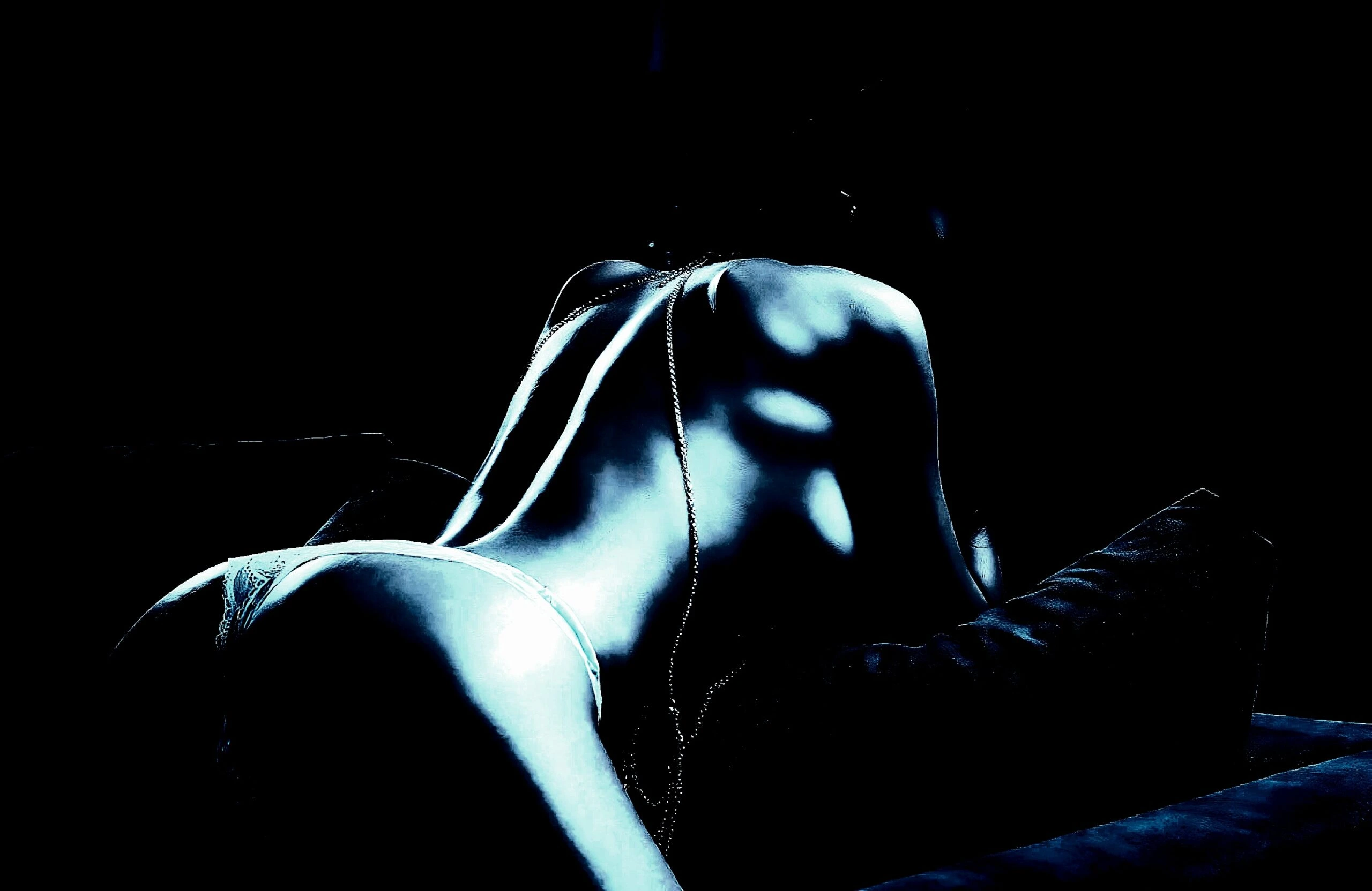 Sensual back view of a woman lying on a couch, showcasing the curves of her back in low, moody lighting.