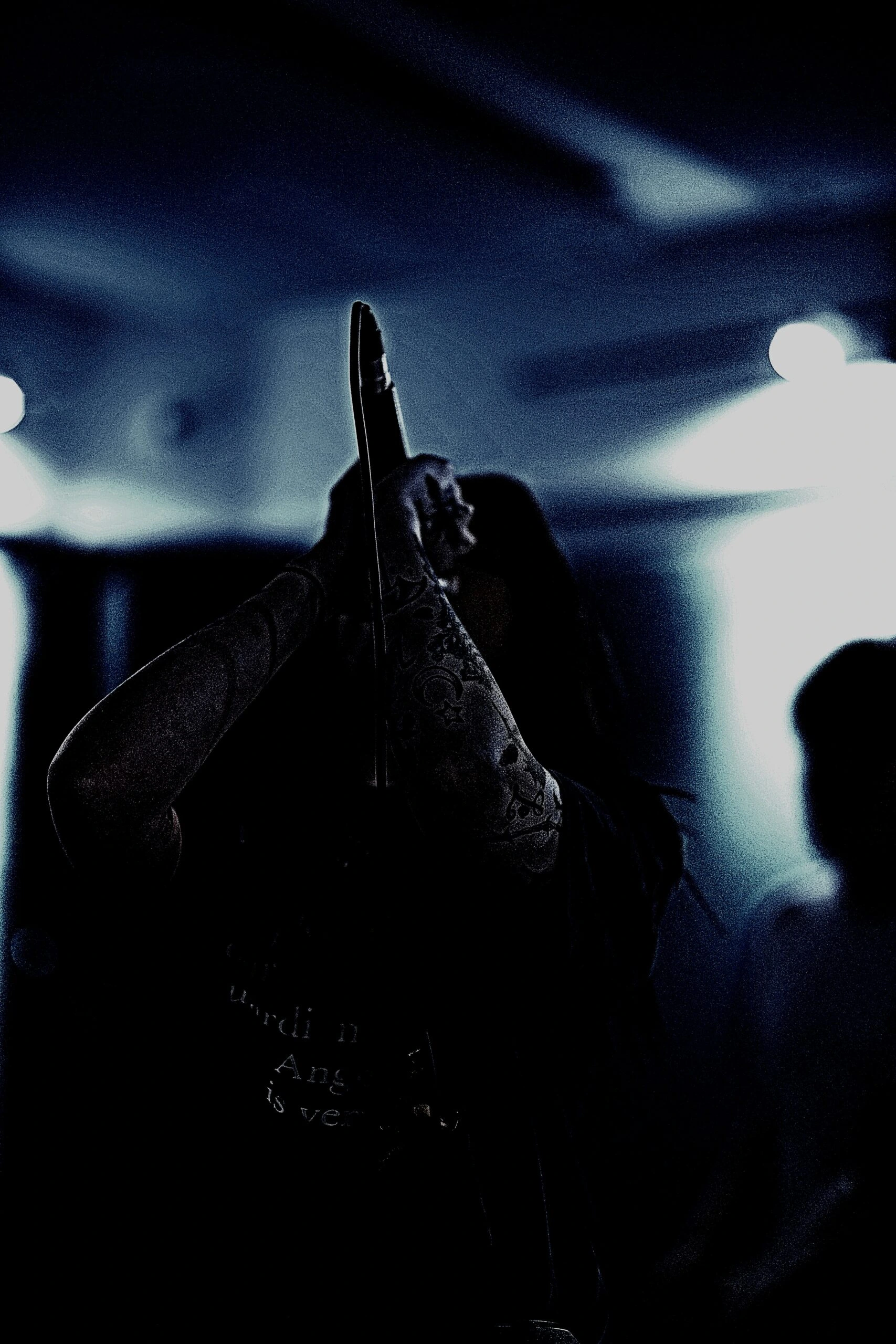 Shadowy scene of a tattooed woman singing into a microphone during a dark, intense live performance.