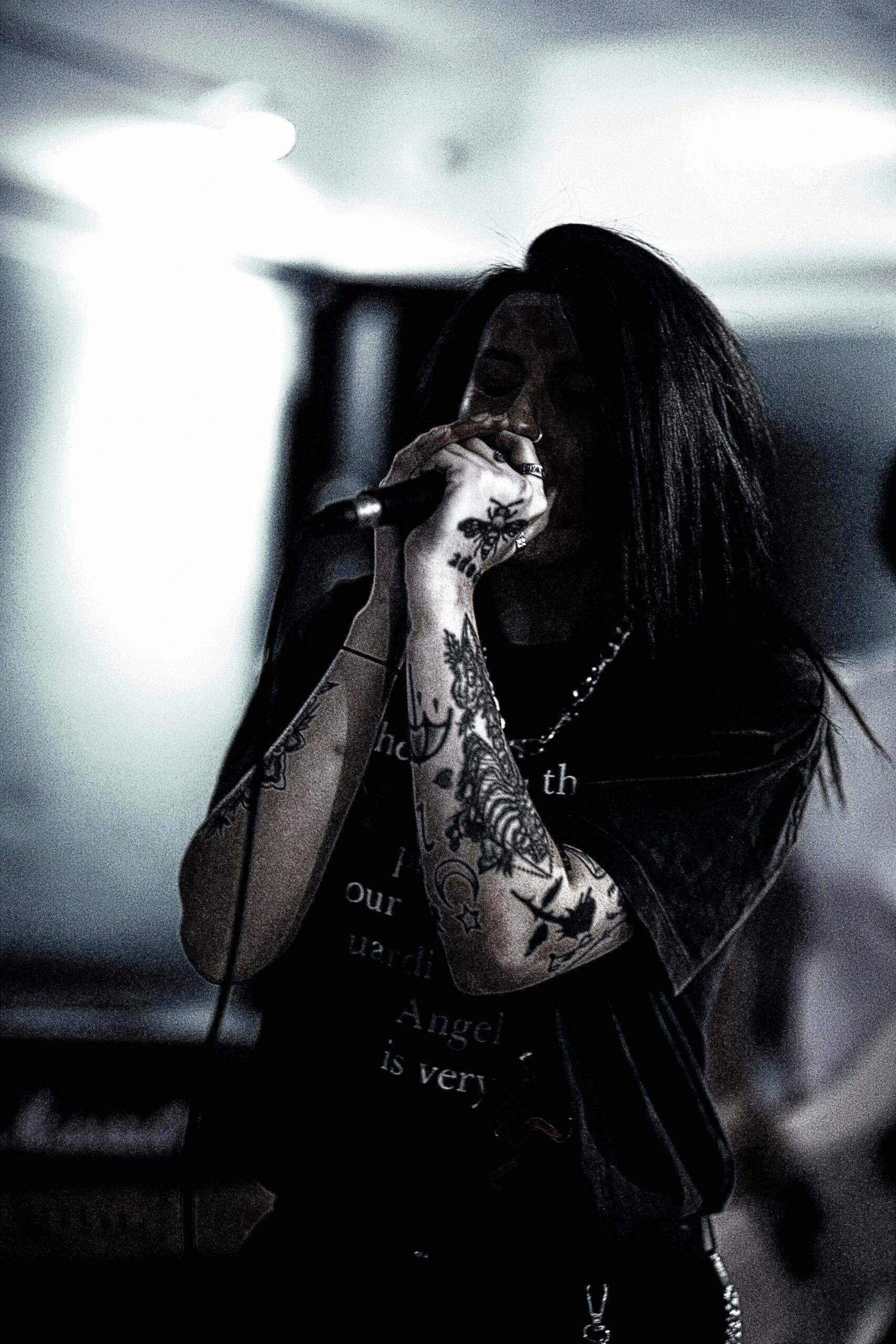 Close-up of a tattooed female singer gripping a microphone passionately, performing in a low-lit, intimate concert setting.