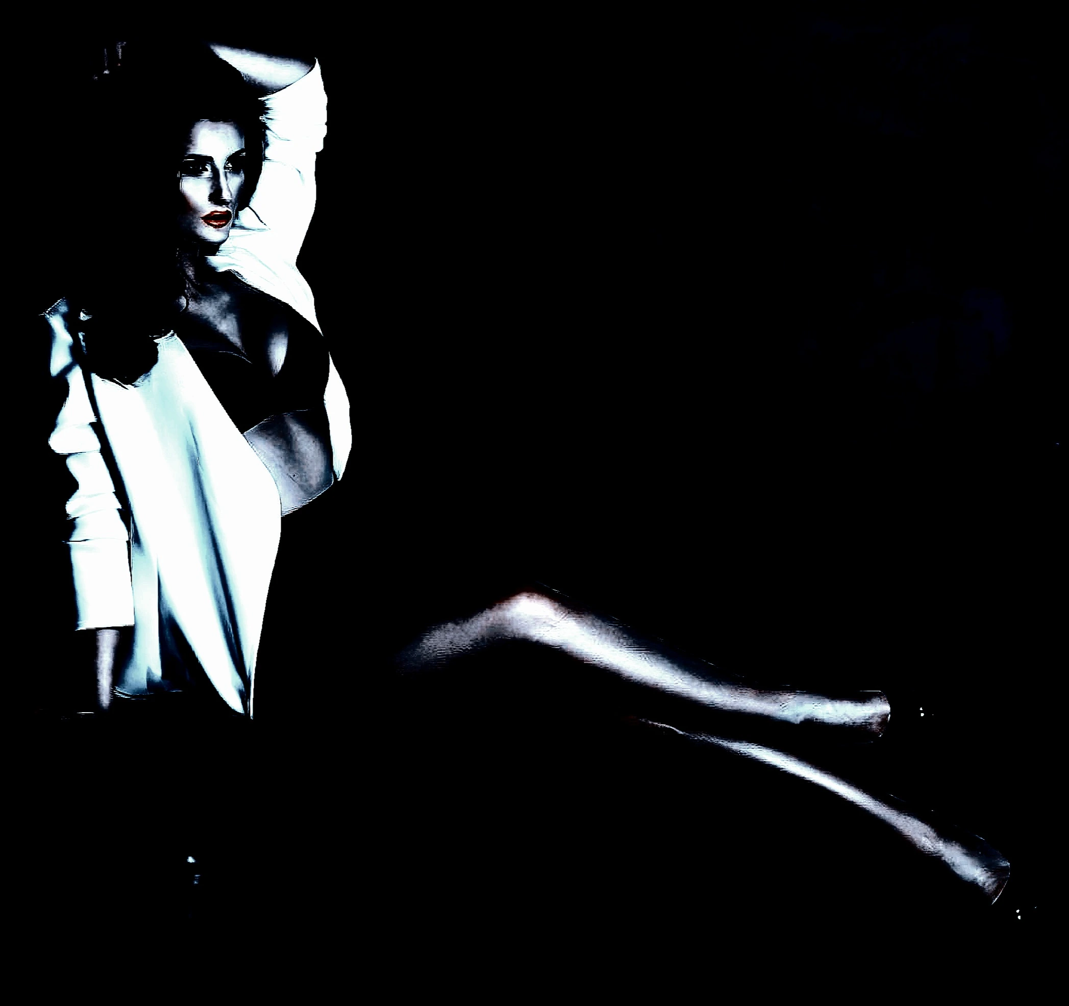 A woman in a black bra and white jacket, reclining seductively against a black backdrop.