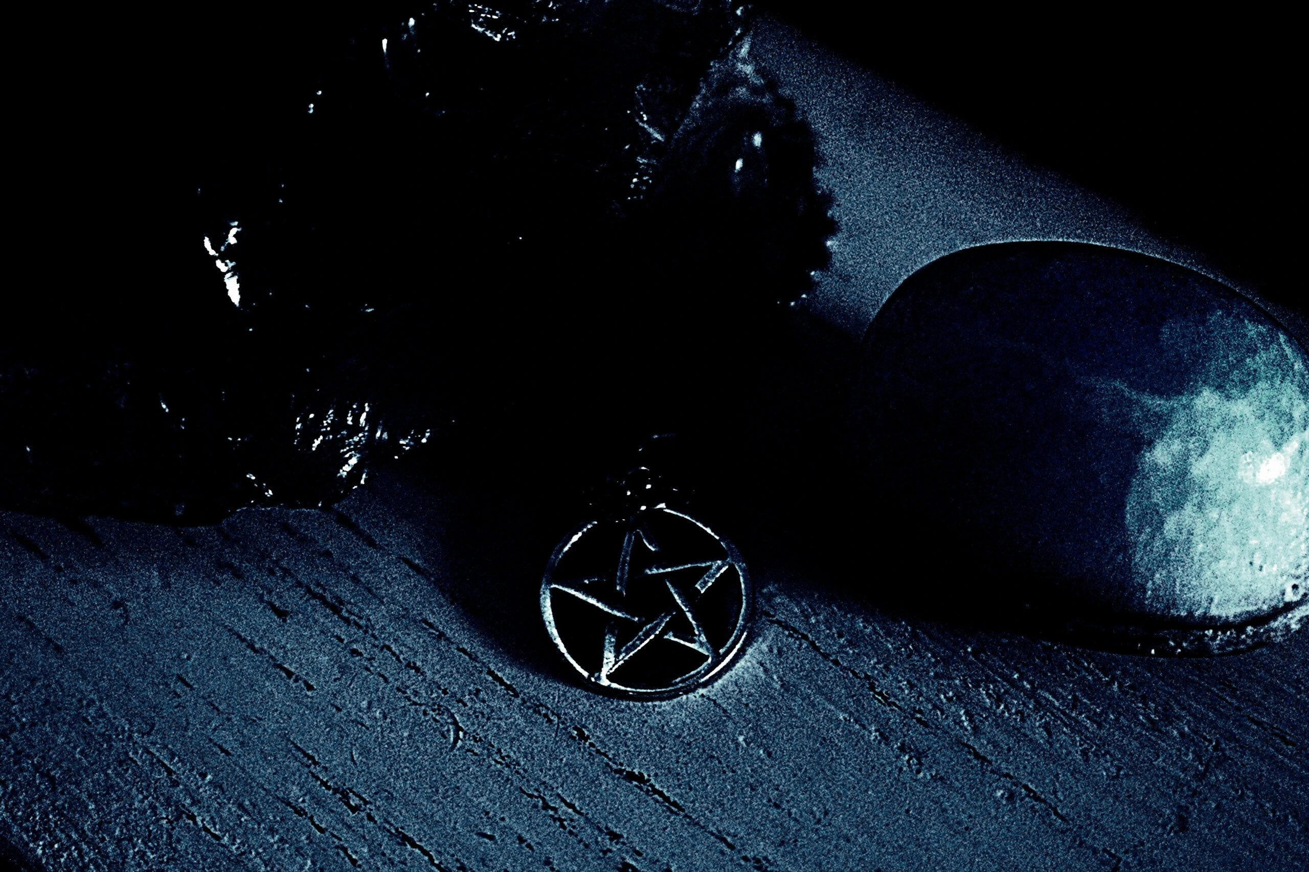 Close-up of a dark pentagram necklace resting on a wooden surface, surrounded by shadows in a gothic, eerie setting.
