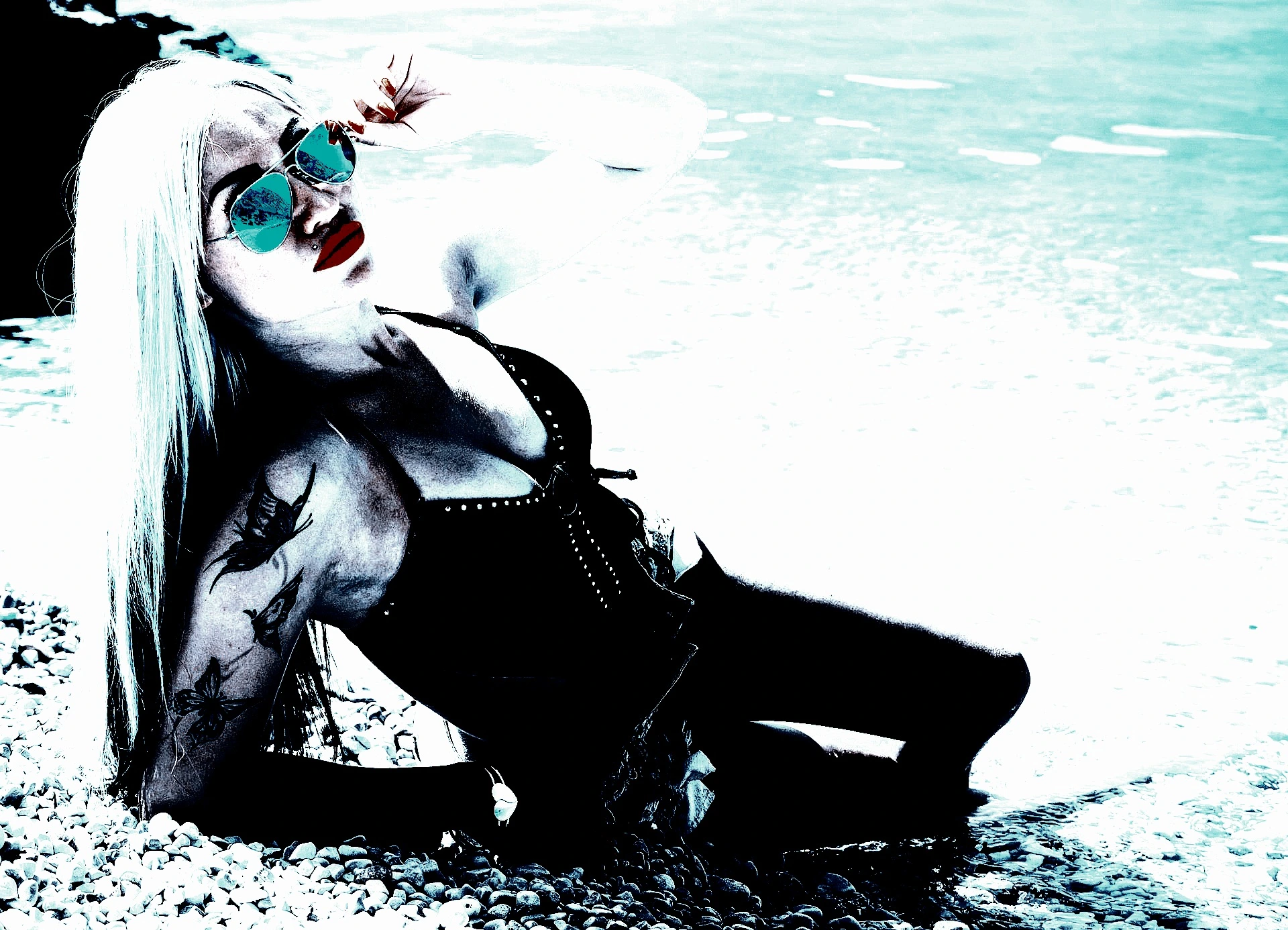 A tattooed woman lounging on the beach in edgy swimwear, wearing reflective aviator sunglasses and sporting bold red lips, blending metalhead style with a seaside vibe.