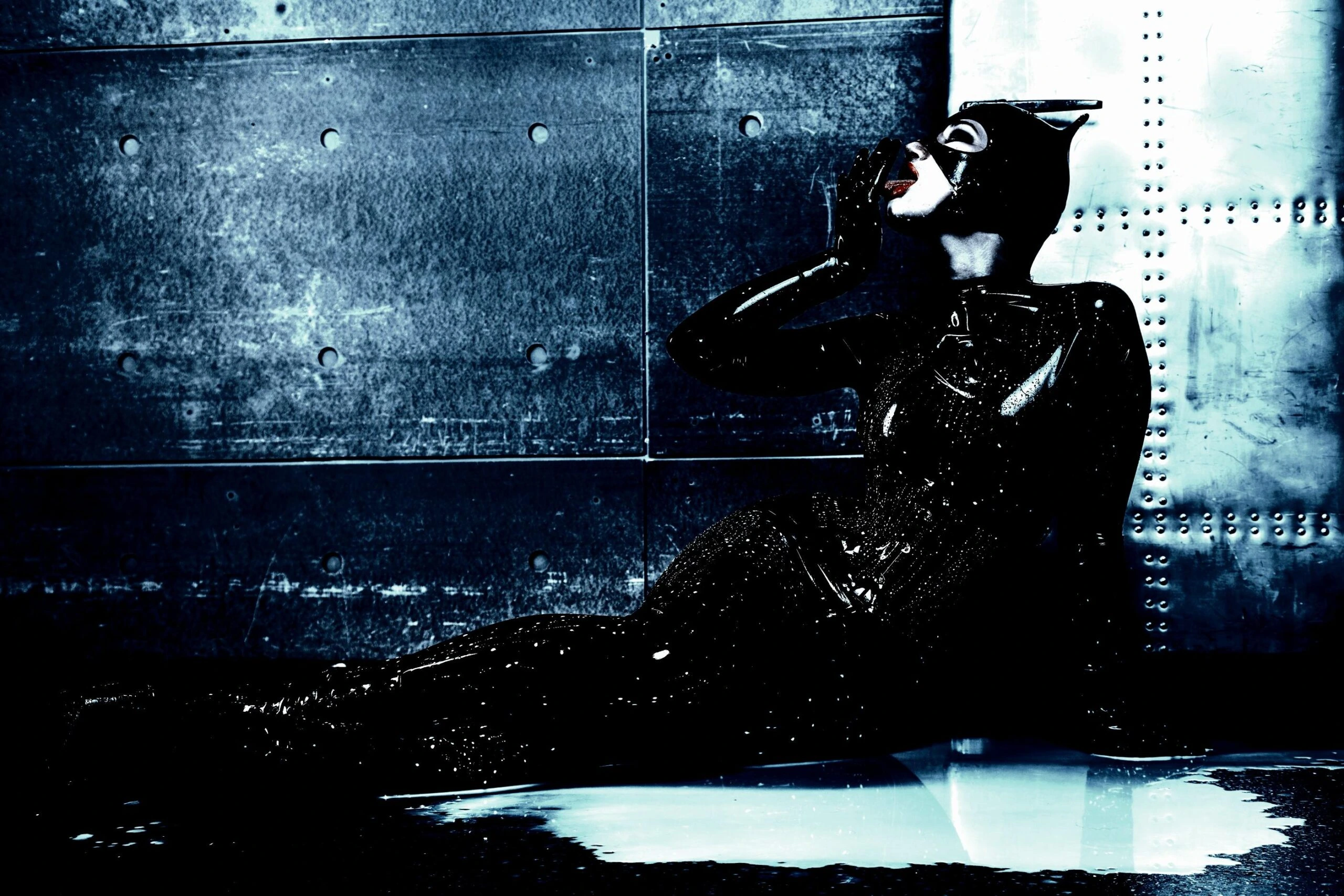 Alternative Catwoman cosplay sitting against a gritty metal wall, reflecting a dark, edgy, and rebellious persona.