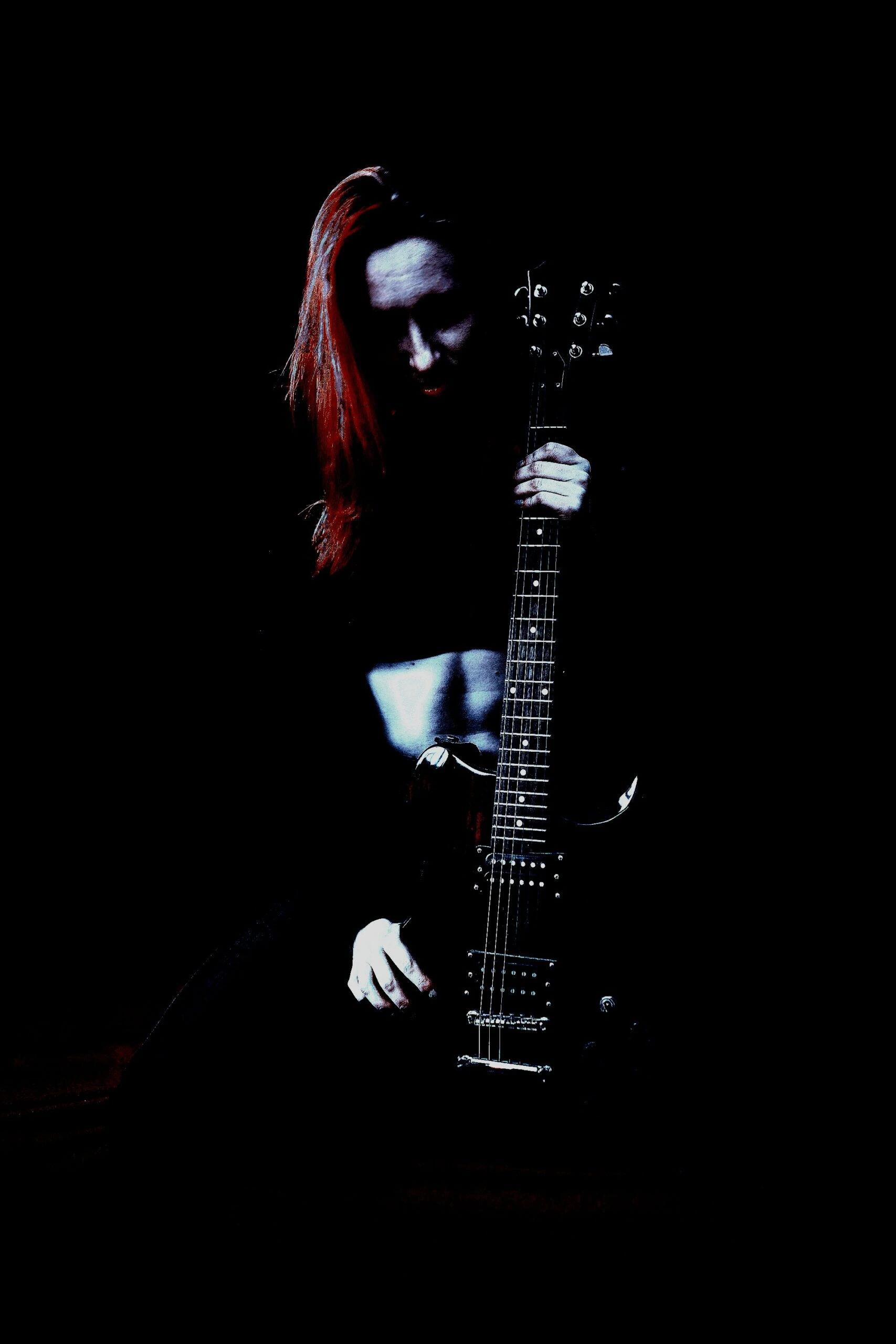 Mysterious woman with red hair, holding an electric guitar under dramatic low lighting, representing dark, alternative vibes and musical intensity.