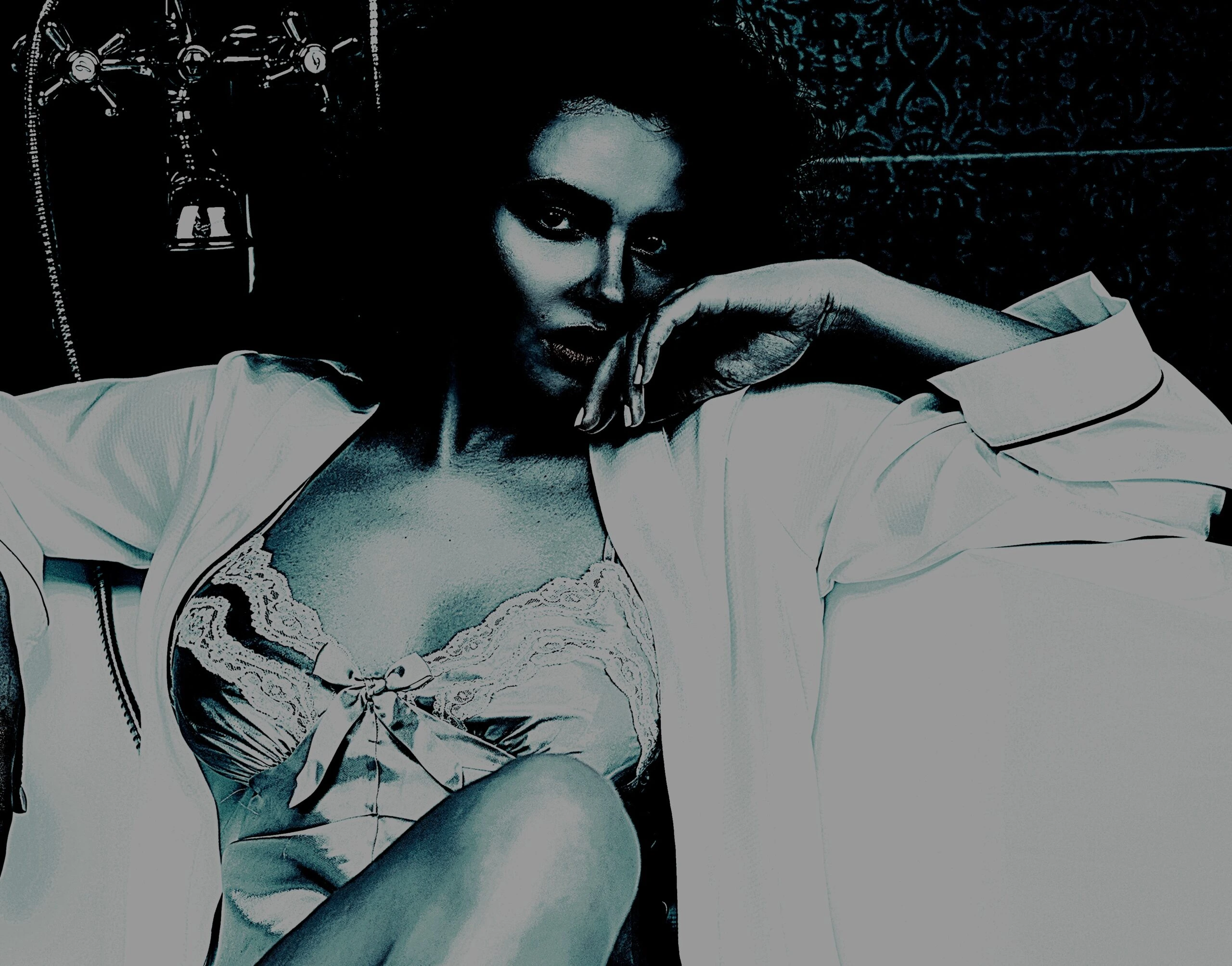 Woman in a satin and lace nightgown leaning against a bathtub, with a thoughtful and alluring expression in dim lighting.