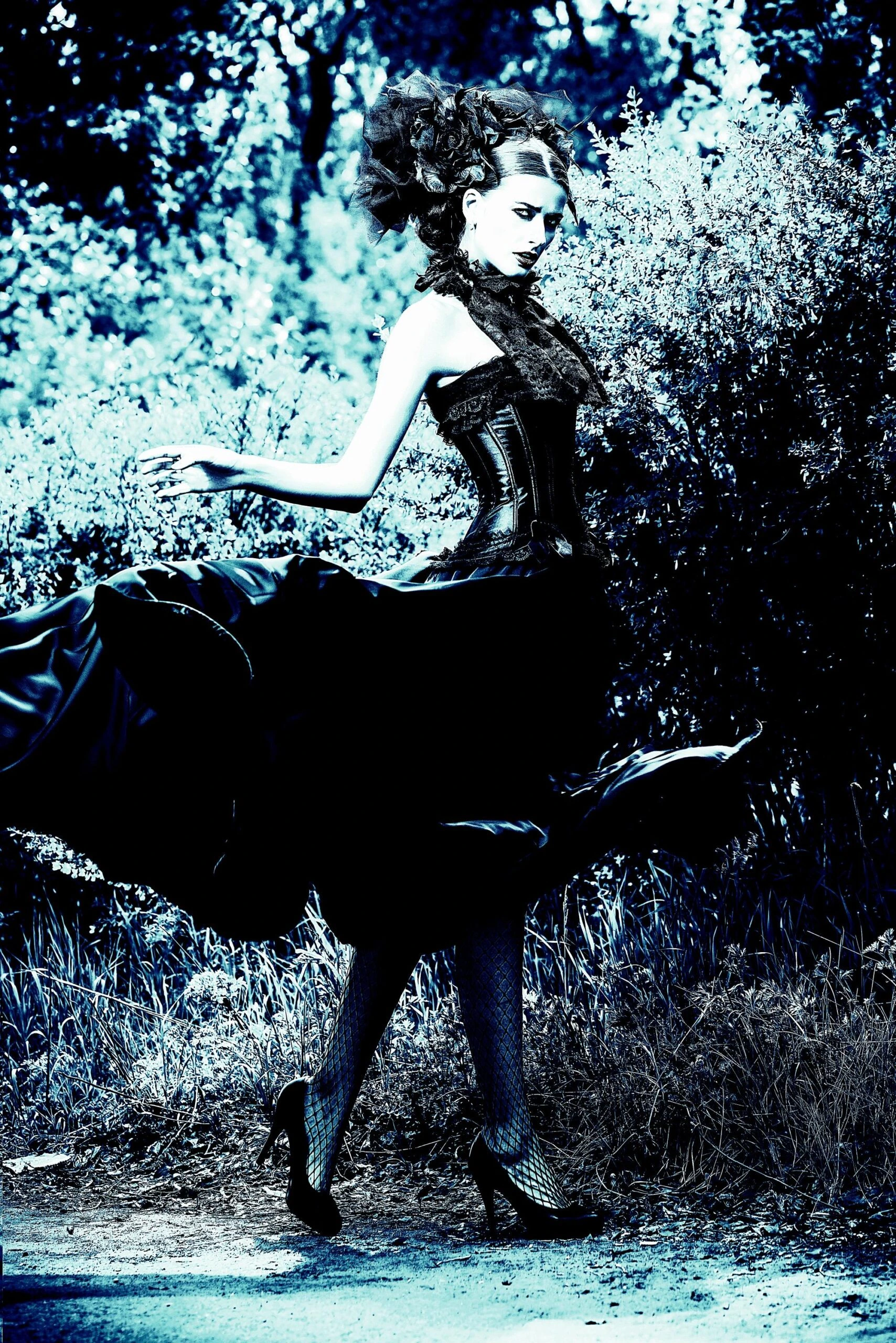 Woman in an elaborate gothic gown with a corset and lace, posing outdoors with a dramatic, flowing skirt.