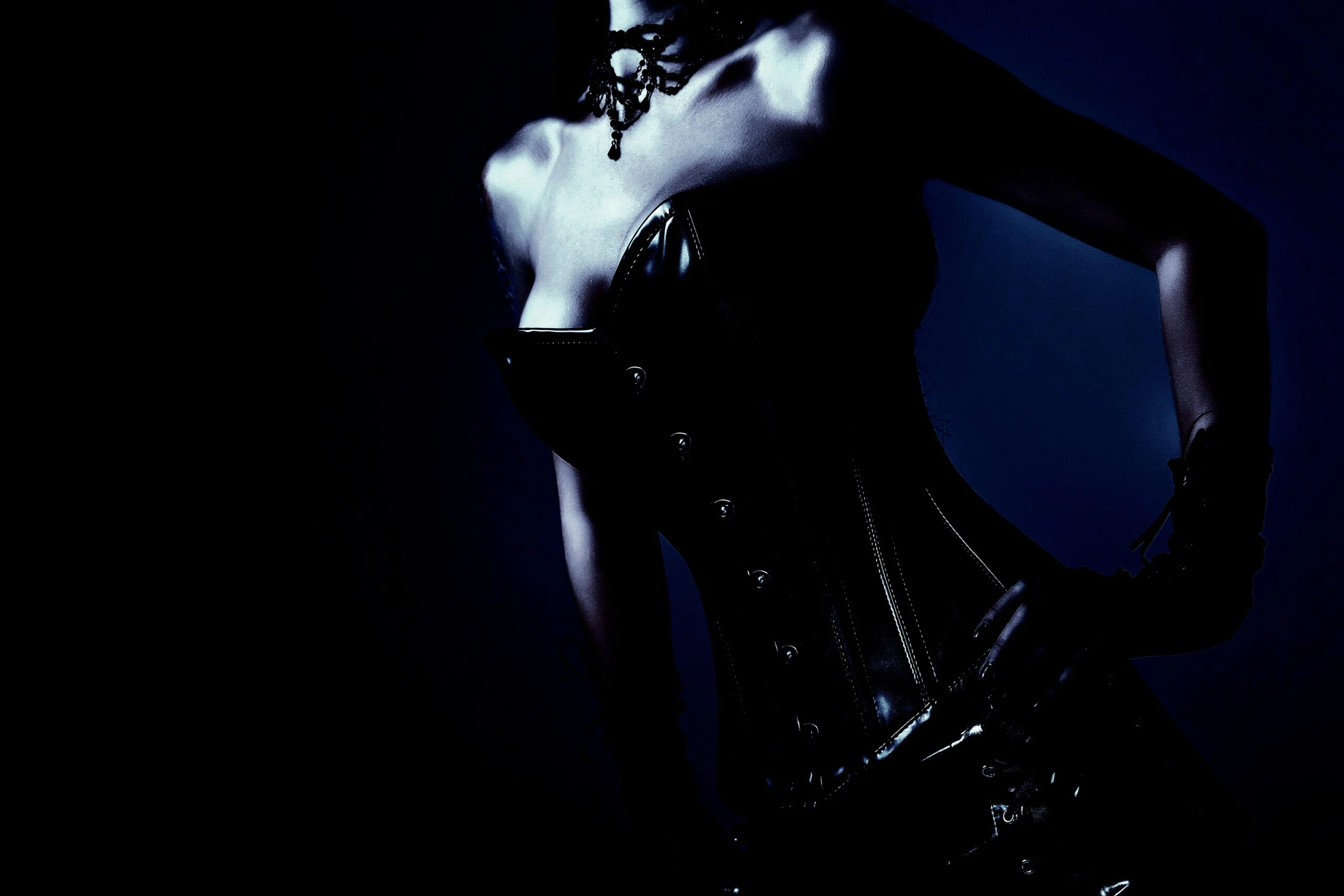 Gothic woman in a dark corset, illuminated dramatically, showcasing elegant neck jewelry in a mysterious atmosphere.