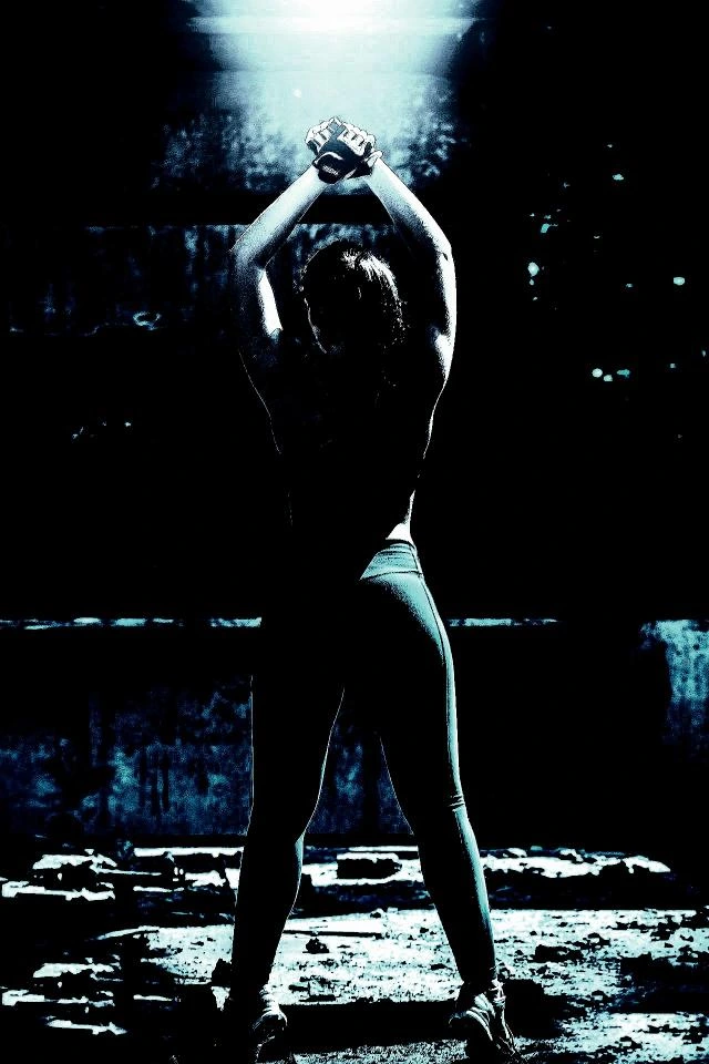 Back view of a woman stretching in a dimly lit industrial setting, highlighting strength and mobility.