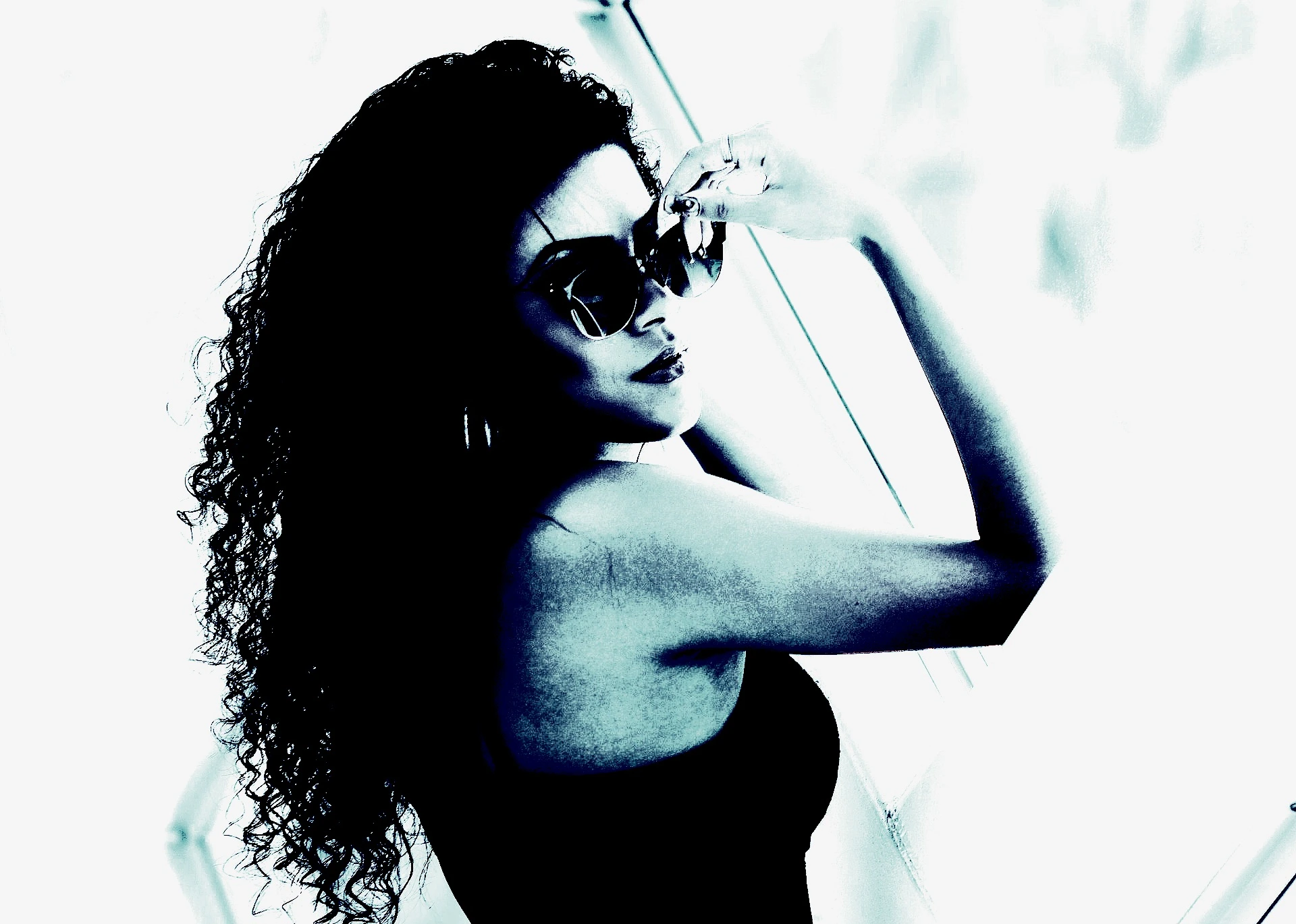 Woman applying red lipstick while wearing large black sunglasses, with a towel wrapped around her head.