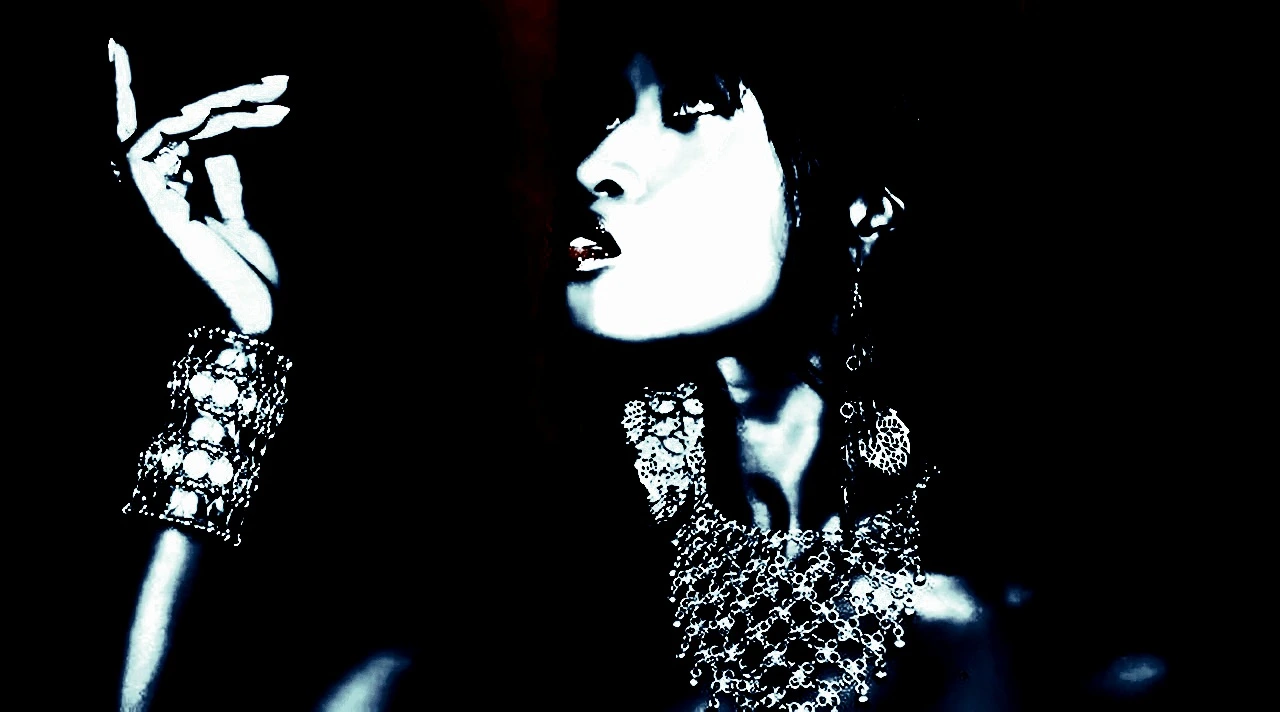 Gothic woman standing by a ladder, wearing dark makeup and black clothing, set against a vibrant blue background.