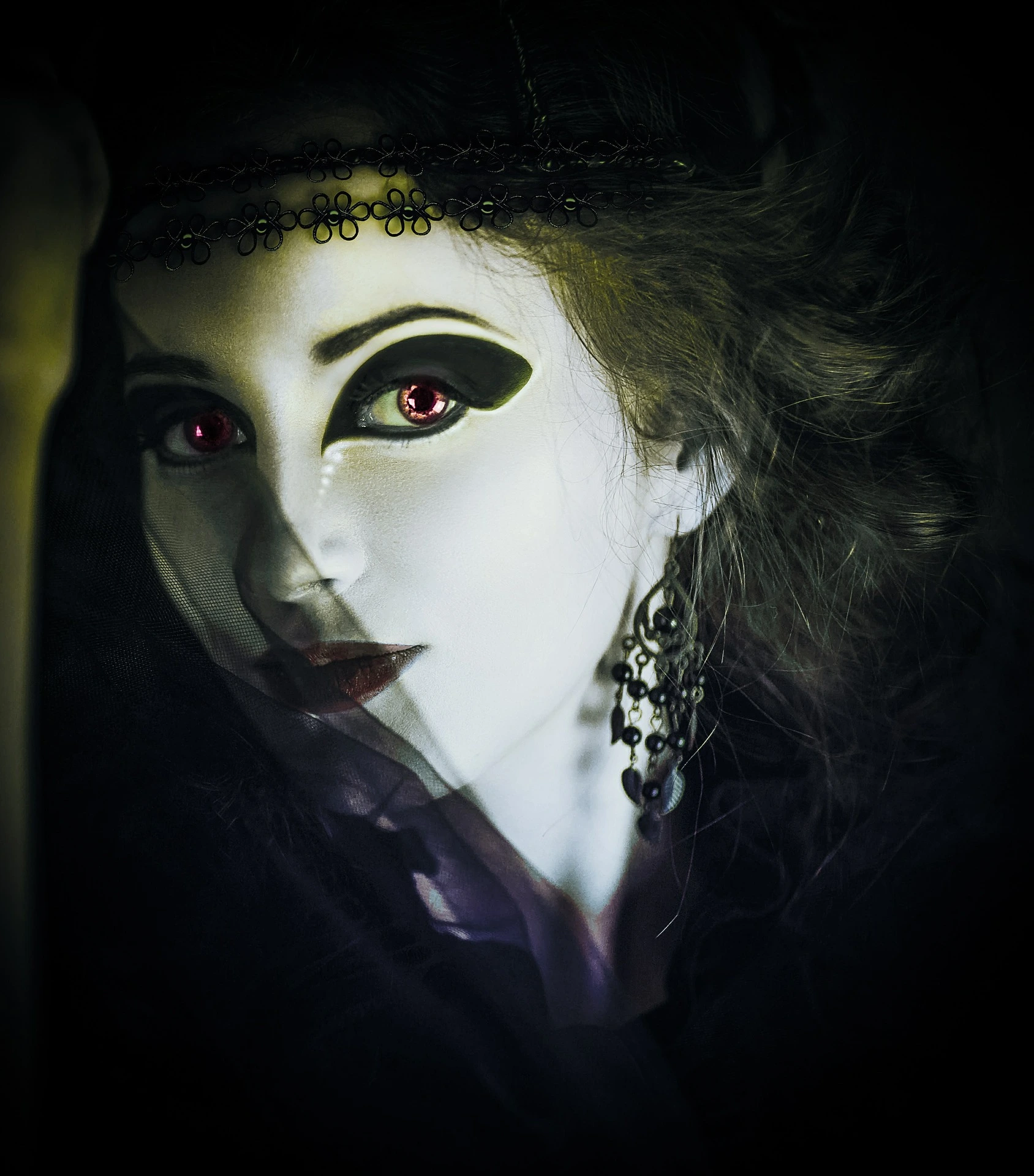 Close-up of a mysterious woman with vampire-inspired makeup and red glowing eyes, adorned with black lace accessories.