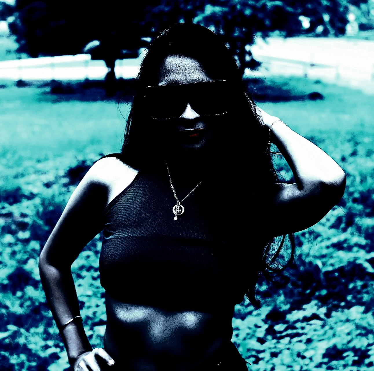 Woman in dark sunglasses and leather jacket, resting her chin on her hands, exuding a goth vibe.
