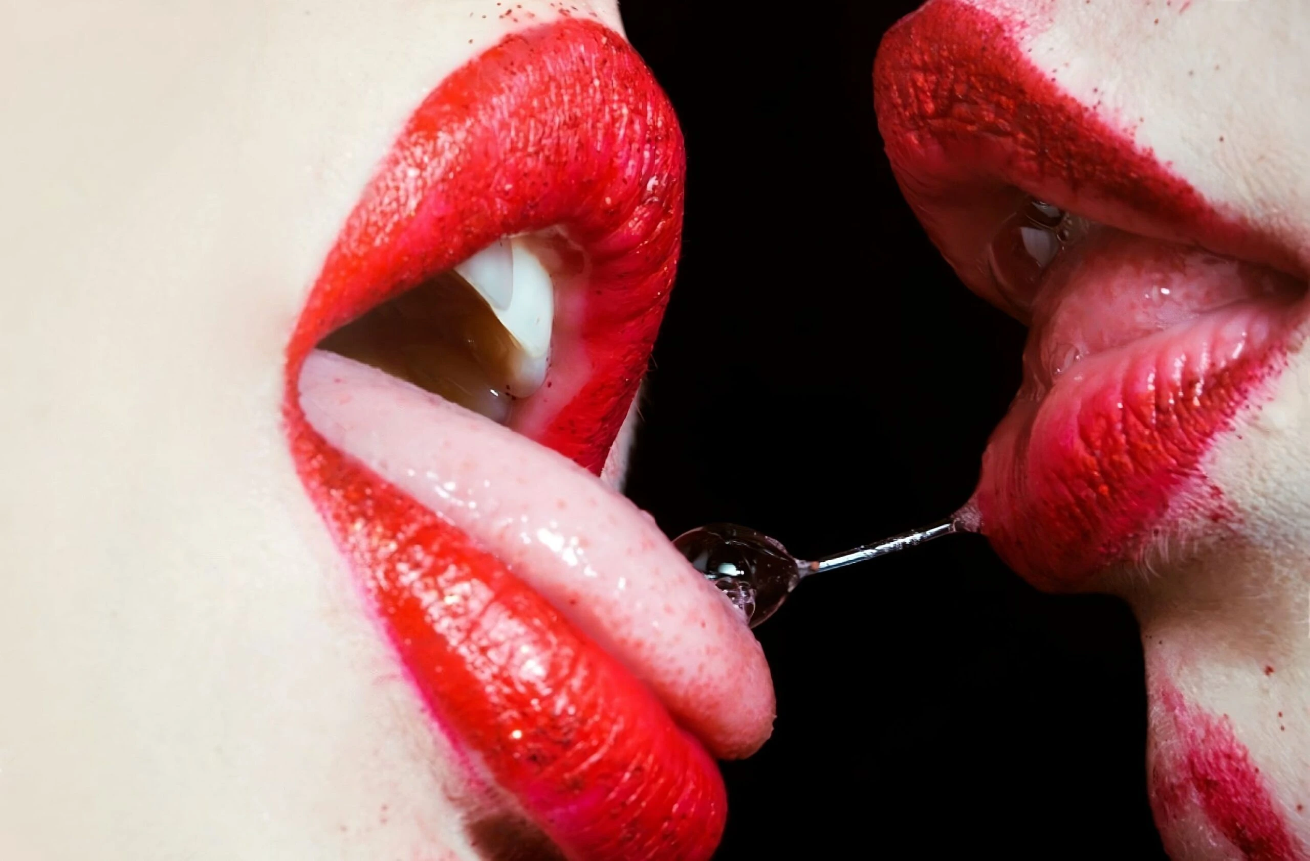 A close-up of two women engaging in a playful and provocative moment, emphasizing the allure of red lipstick.